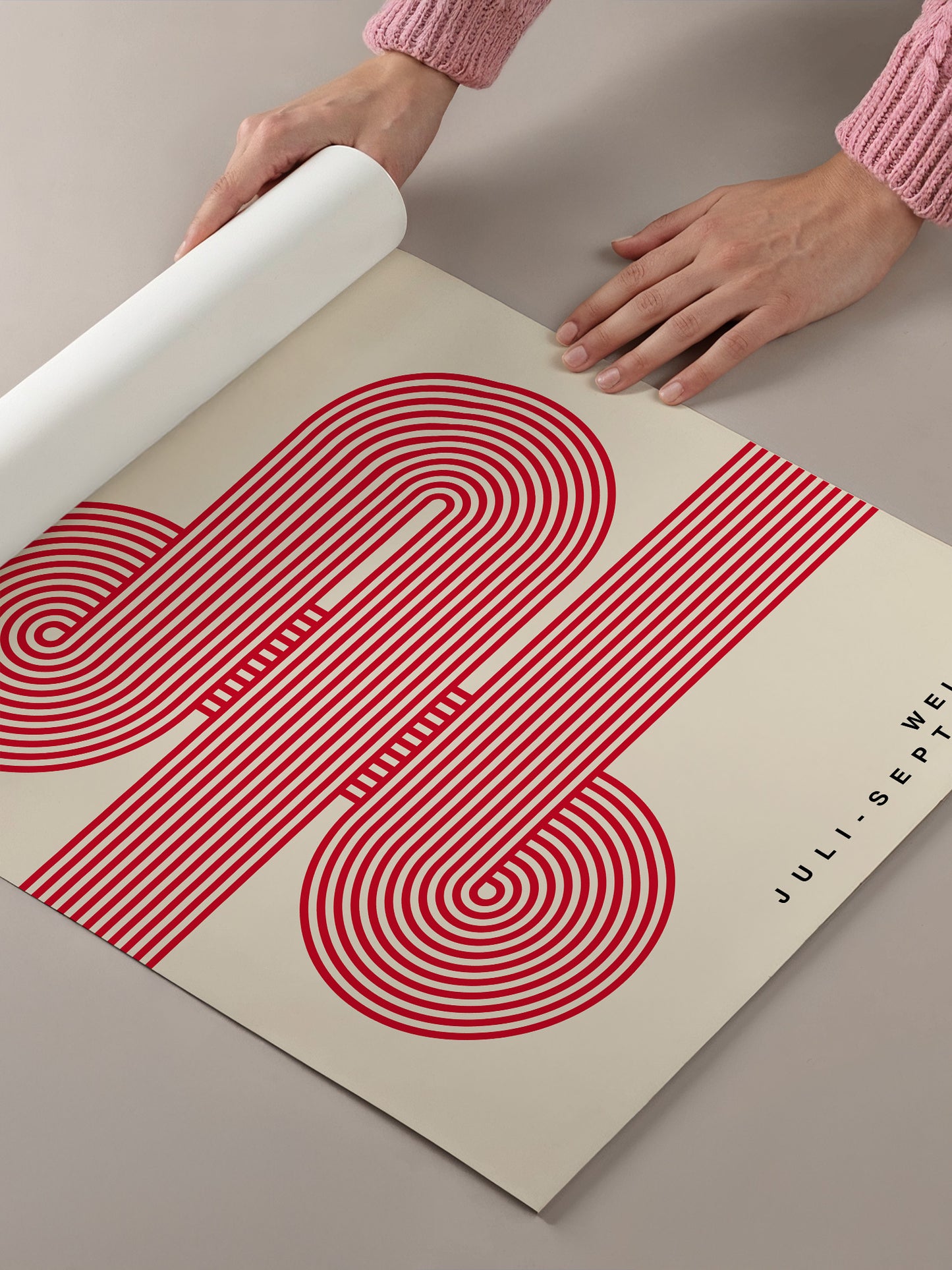A person's hands are holding a roll of paper with a large, abstract red and white design featuring concentric circles and lines.