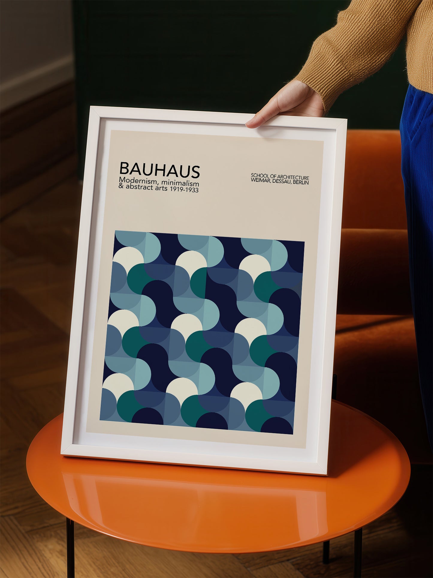 A person is holding a framed poster of the Bauhaus art school, featuring a geometric pattern in shades of blue and white.