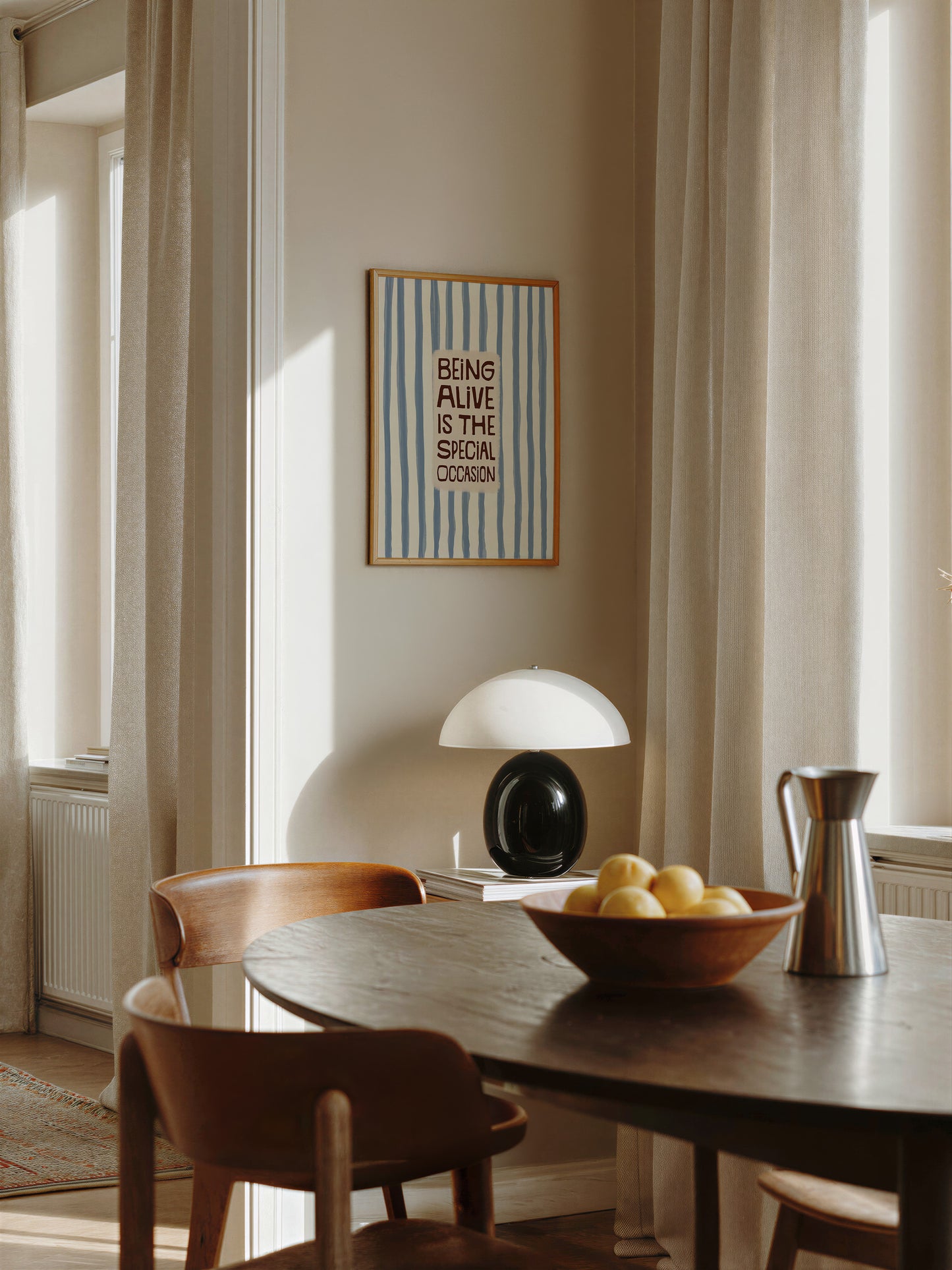 a cozy dining area with a wooden table, two chairs, and a bowl of fruit. A framed quote on the wall says "Being alive is the special occasion".