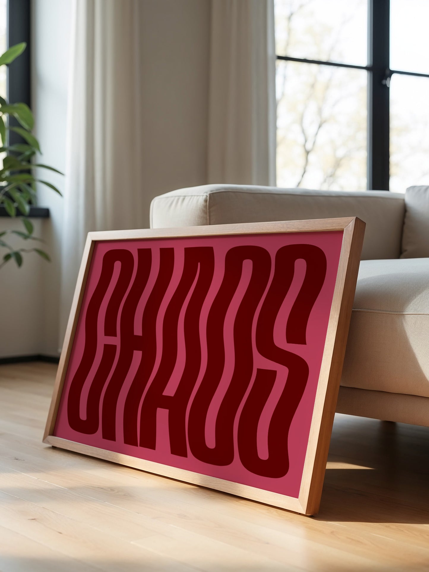 A framed poster with the word "CHAOS" in large, bold red letters is displayed on a wooden floor in a room with a window.