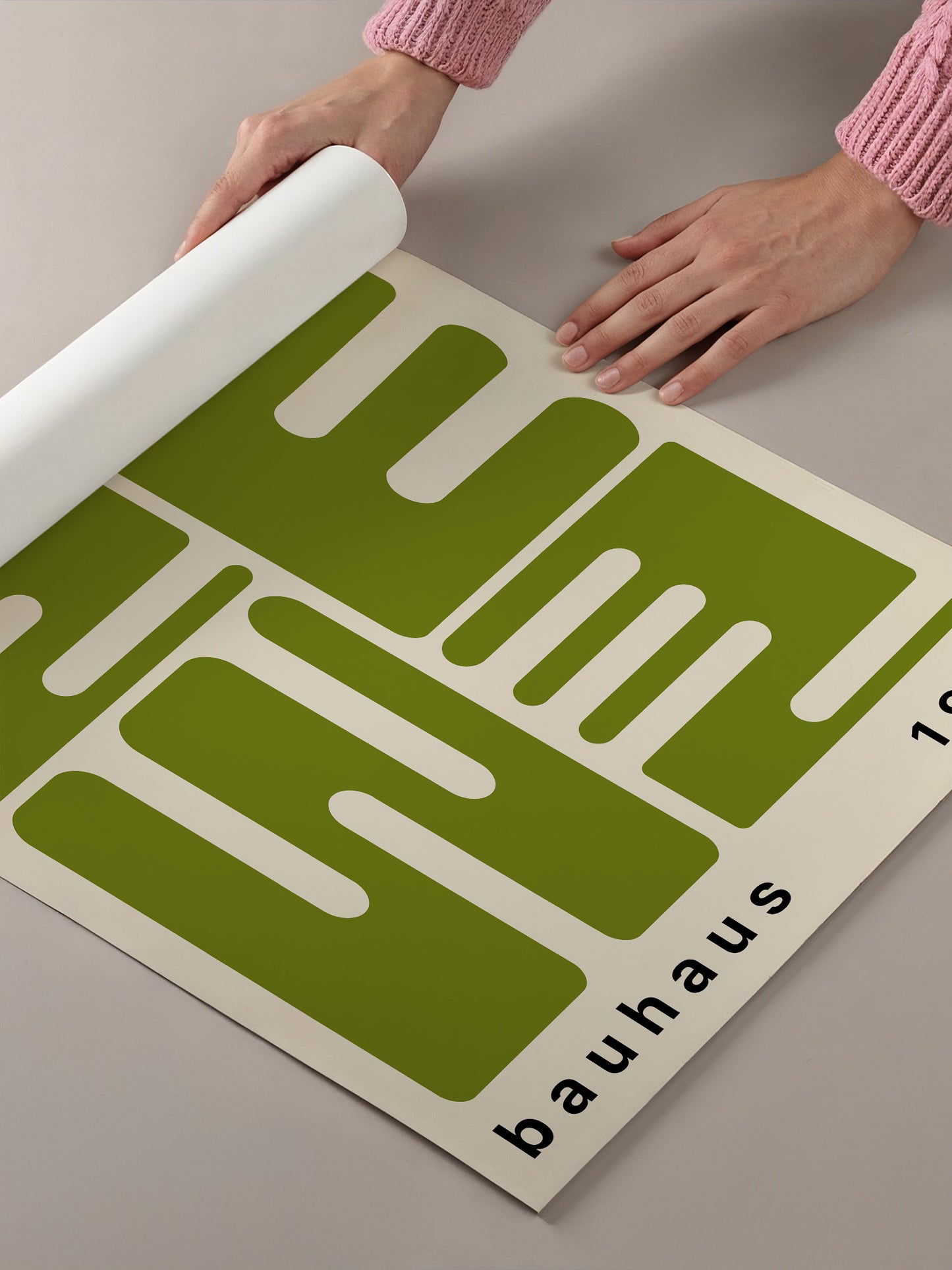 A person's hands are holding a roll of paper, which appears to be a poster or artwork featuring a large green geometric design.