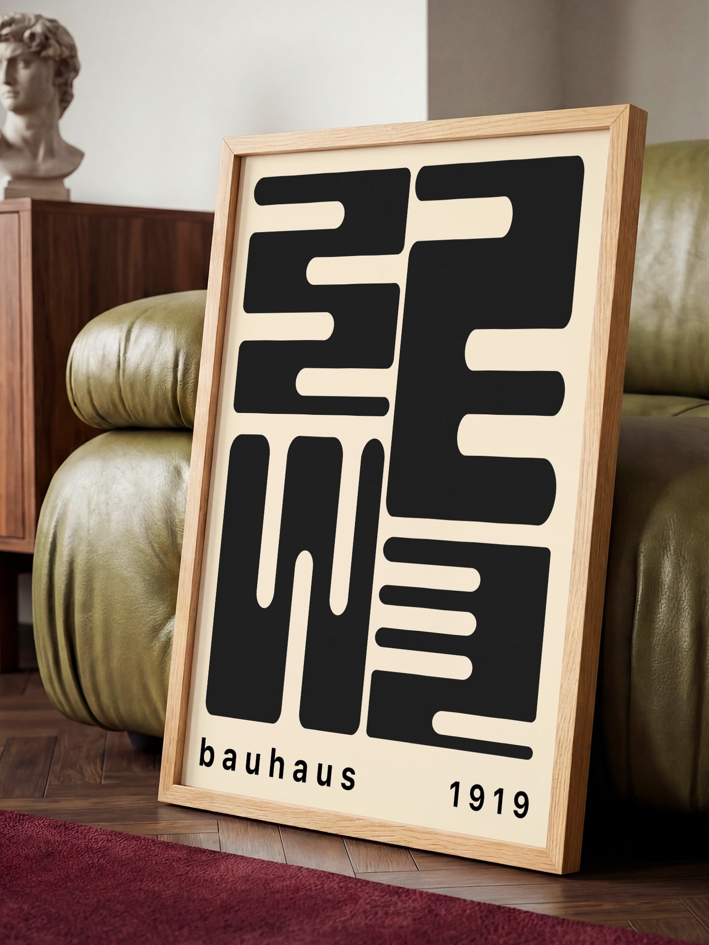 A framed poster with a minimalist design featuring bold black text and geometric shapes, placed on a wooden floor in a room with a green leather couch.