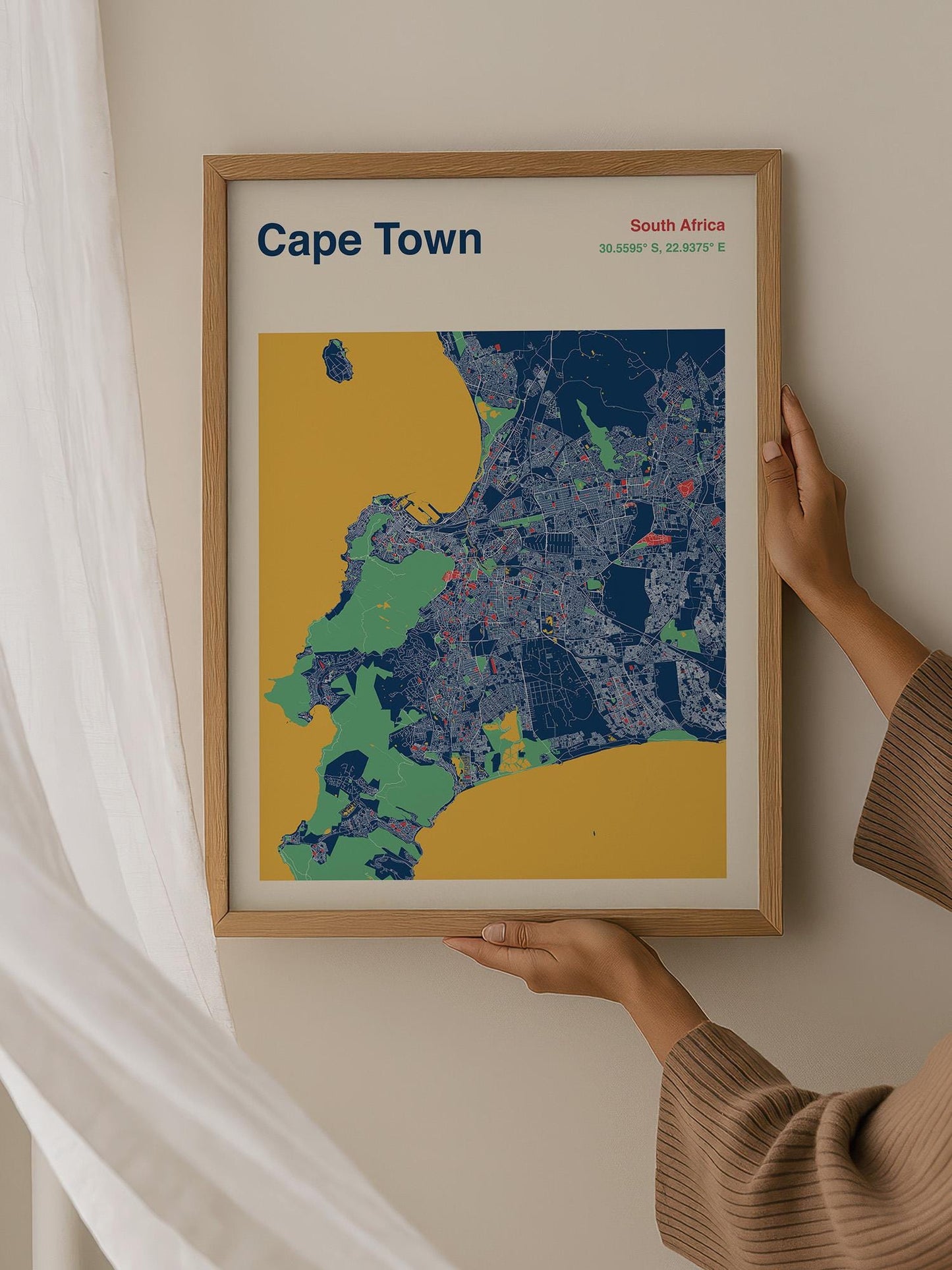 A person is holding up a framed map of Cape Town, South Africa, which is a colorful and detailed representation of the city.