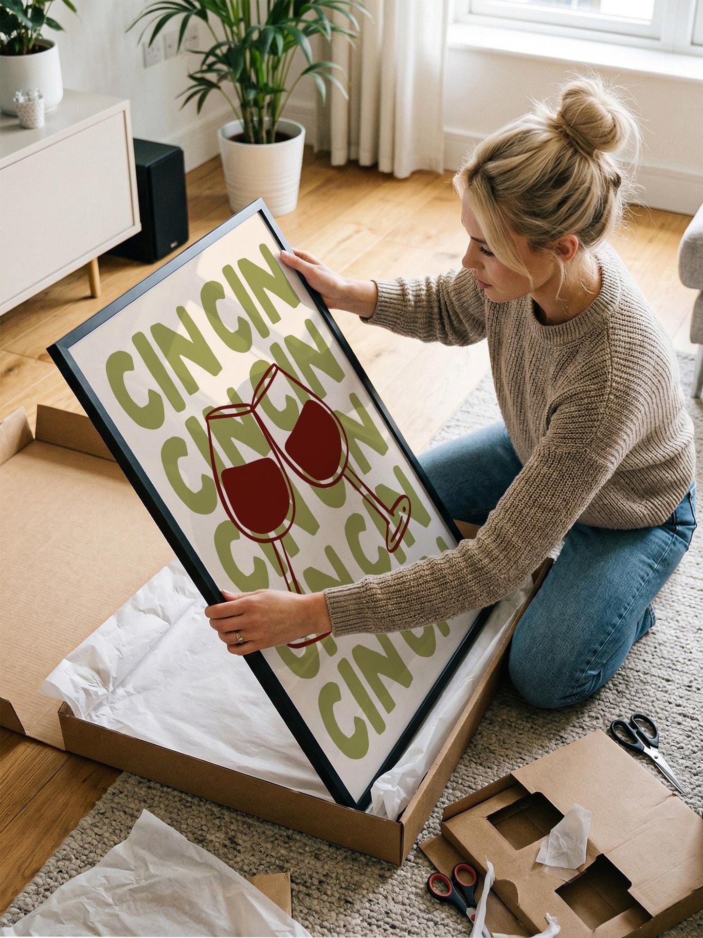 A woman is kneeling on the floor and holding a framed poster with the word "CINNAMON" on it.