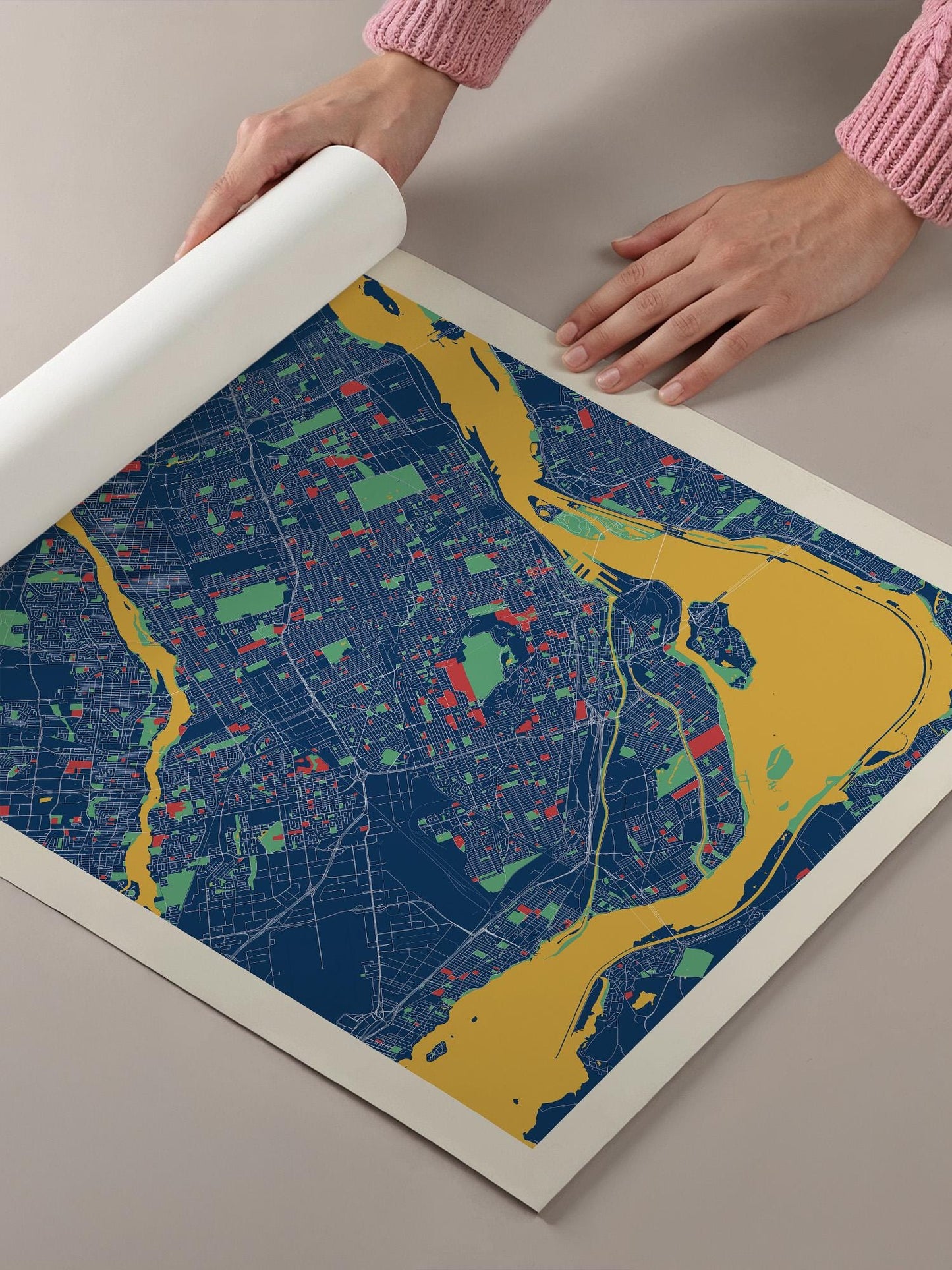A person's hands are holding a roll of paper over a colorful map of a city, which appears to be a detailed and vibrant representation of the urban landscape.