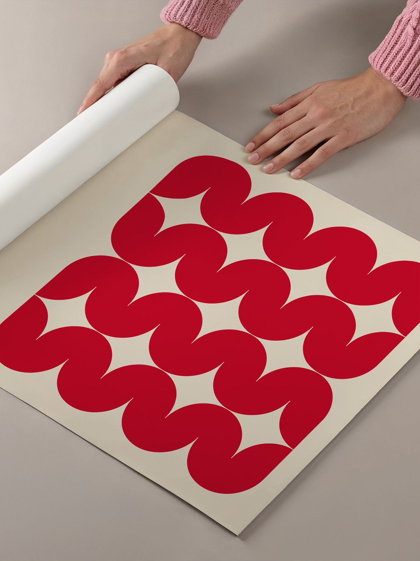 A person's hands are holding a roll of paper, which is laid out on a table with a pattern of red circles on it.