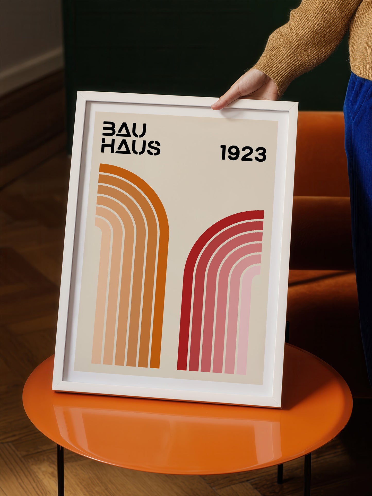 A person is holding a framed poster with the text "BAU HAUS 1923" and two abstract geometric designs in different colors.