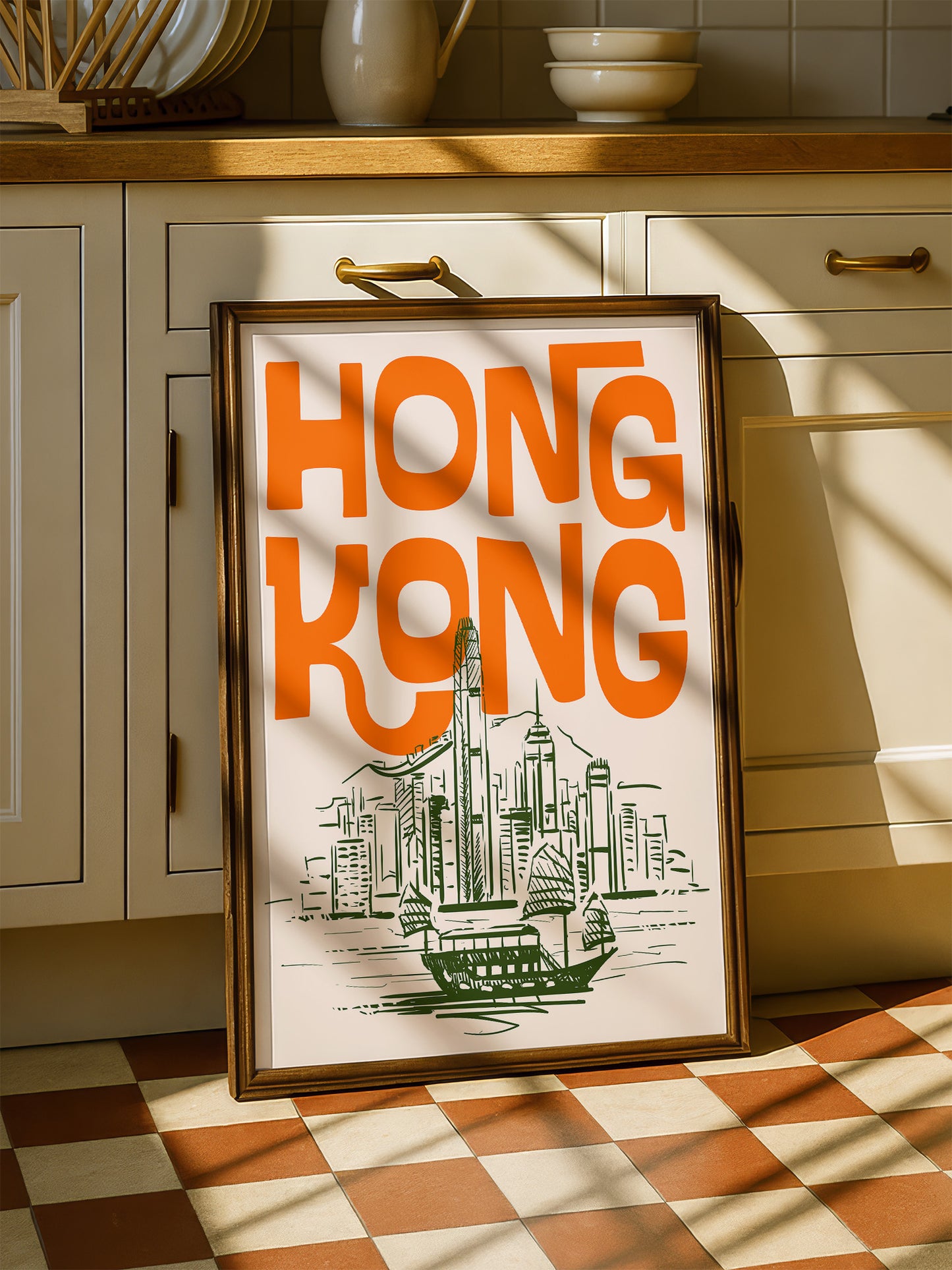 A framed poster of Hong Kong with an illustration of the city skyline is displayed on a checkered floor in a kitchen.