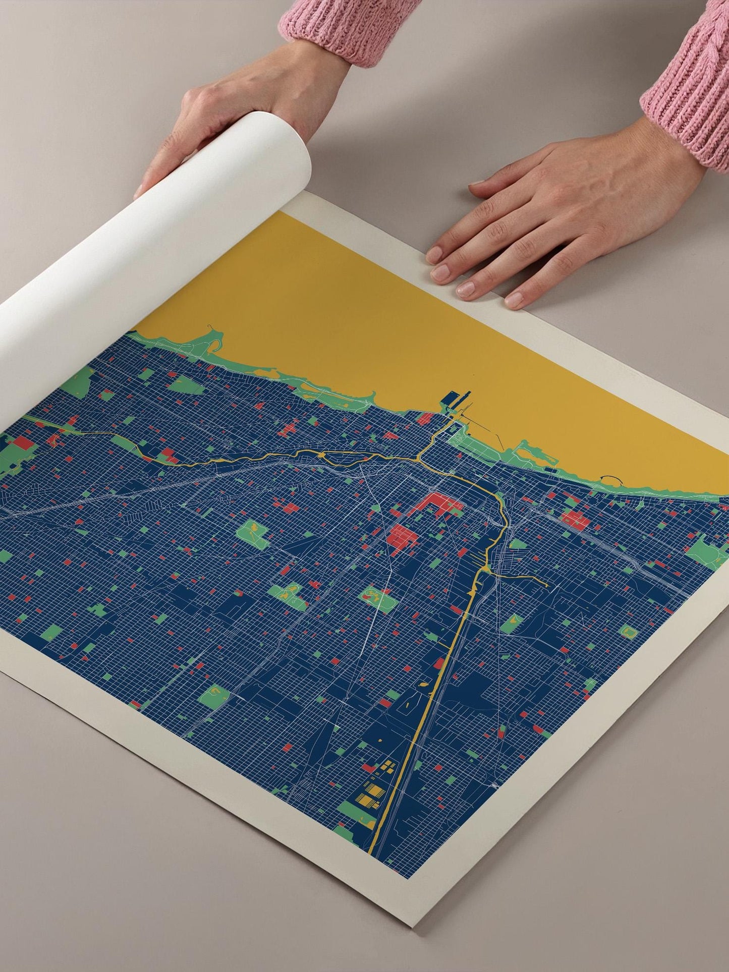 A person's hands are holding a roll of paper over a colorful map of a city, which appears to be a detailed and intricate representation of the urban landscape.