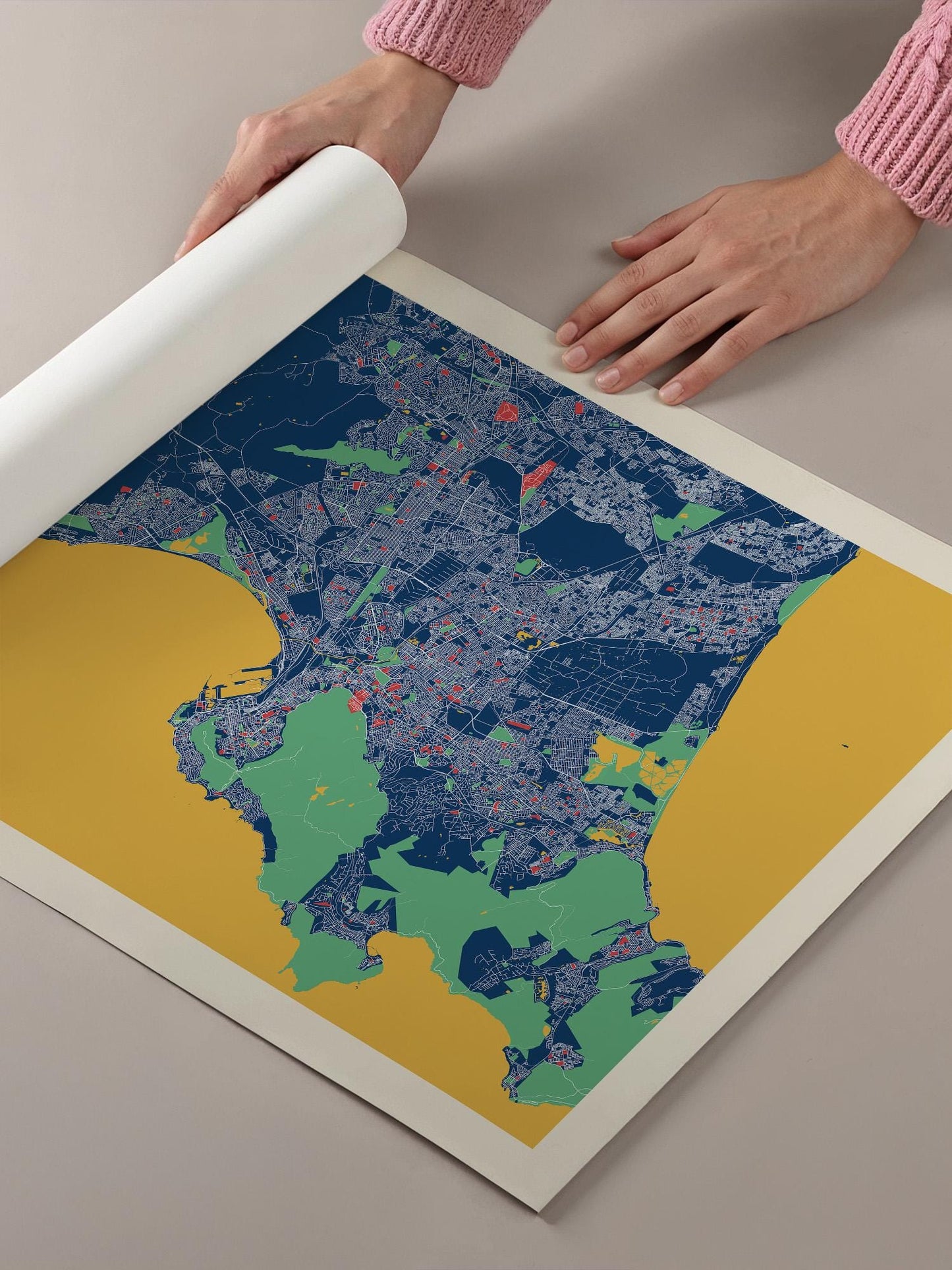 A person's hands are holding a roll of paper over a colorful map of a city, which appears to be a detailed and vibrant representation of the urban landscape.