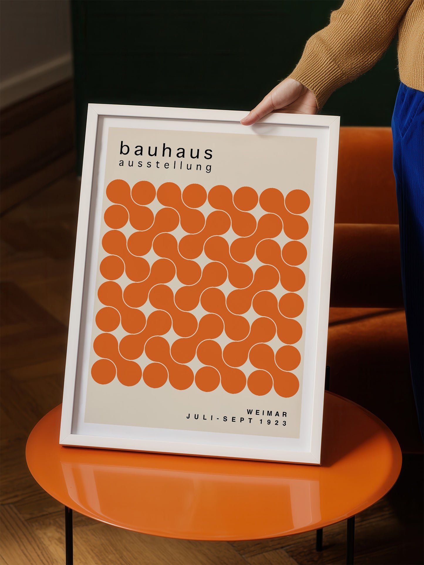 A person is holding a framed poster with a repeating pattern of orange circles on a white background.