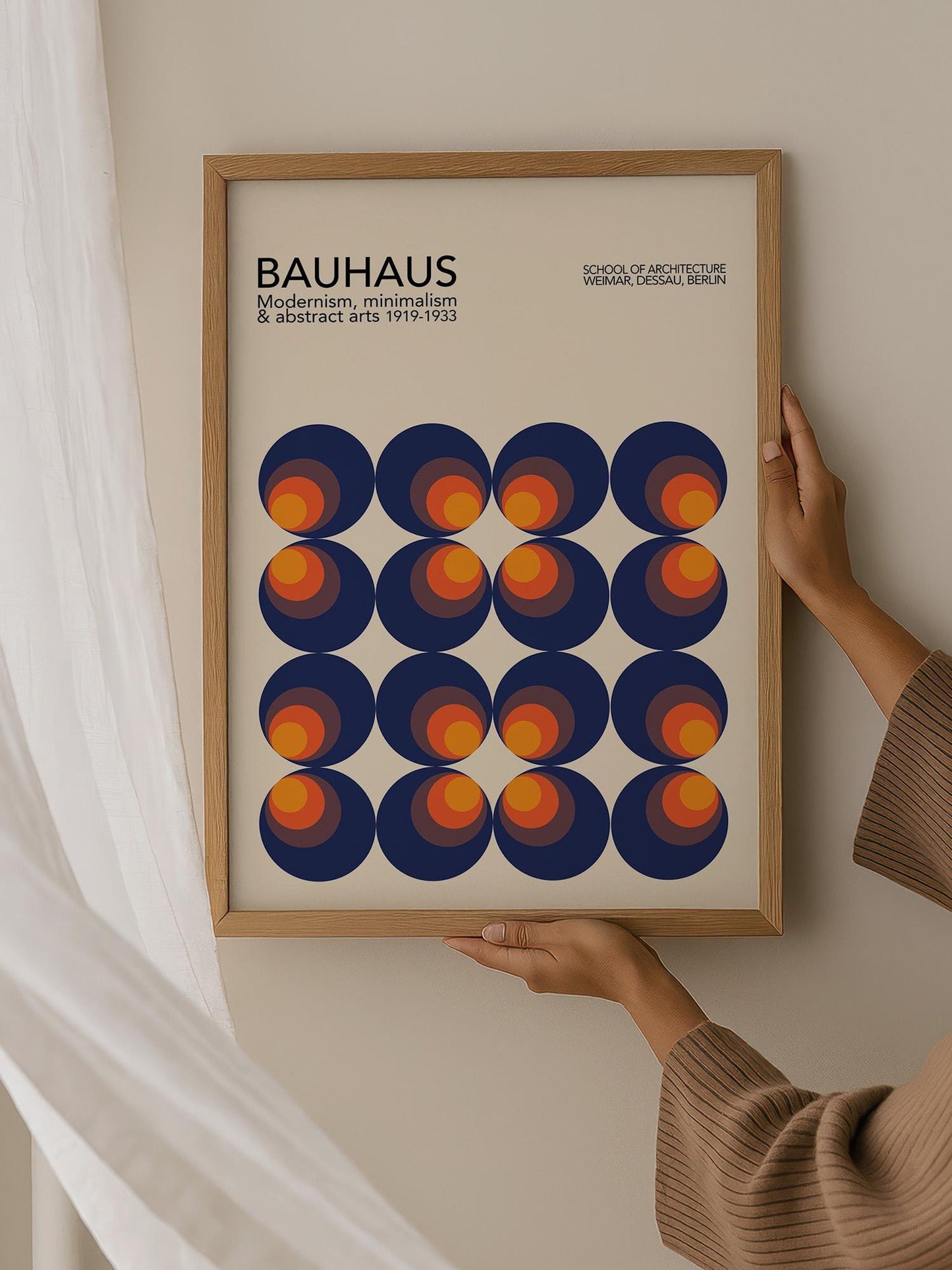 A person is holding up a framed poster of a Bauhaus-style abstract artwork featuring a repeating pattern of circles in various shades of blue, orange, and yellow.