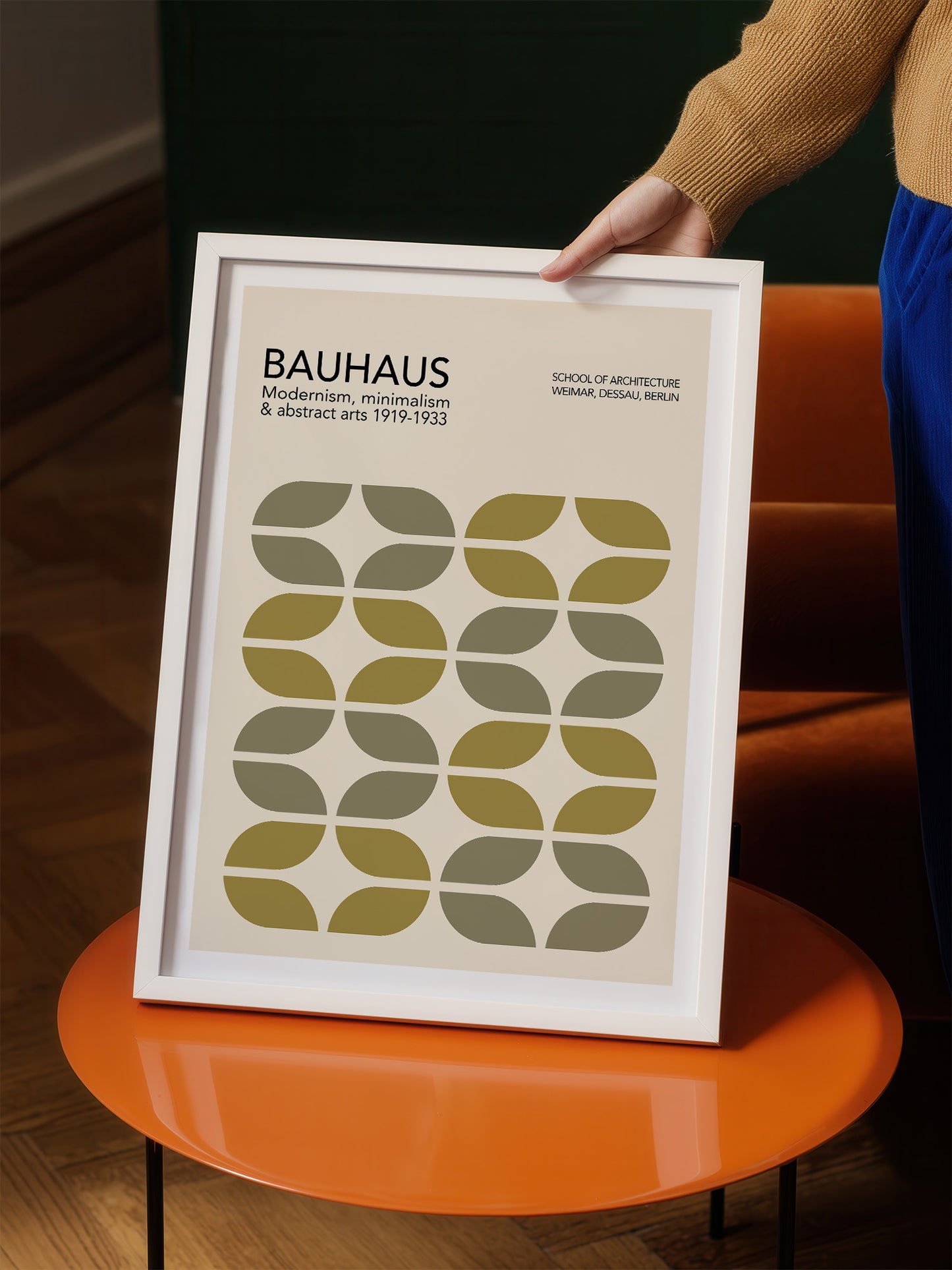 A person is holding a framed poster of the Bauhaus art school, featuring a minimalist design with geometric shapes in shades of green and brown.