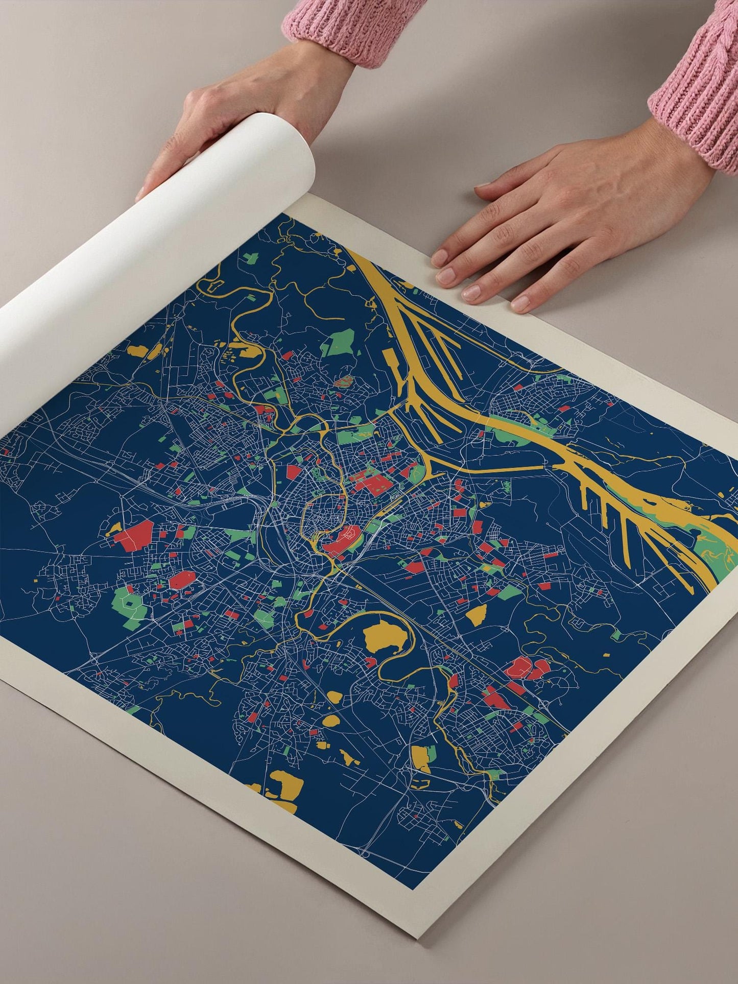 A person's hands are holding a roll of paper over a colorful map of a city, which appears to be a detailed and intricate representation of the urban landscape.
