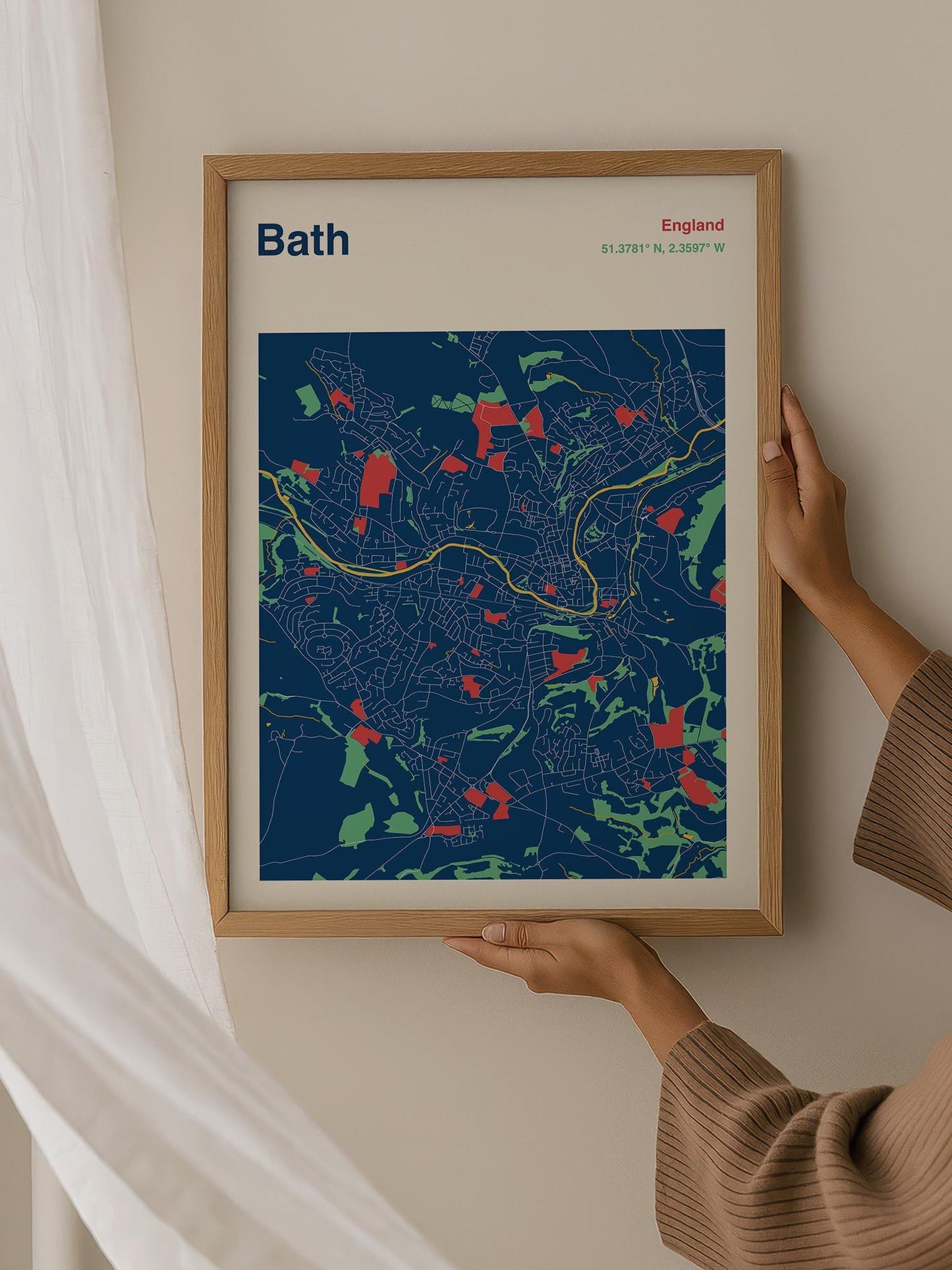 A person is holding up a framed map of Bath, England, which features a colorful and detailed representation of the city's streets and landmarks.