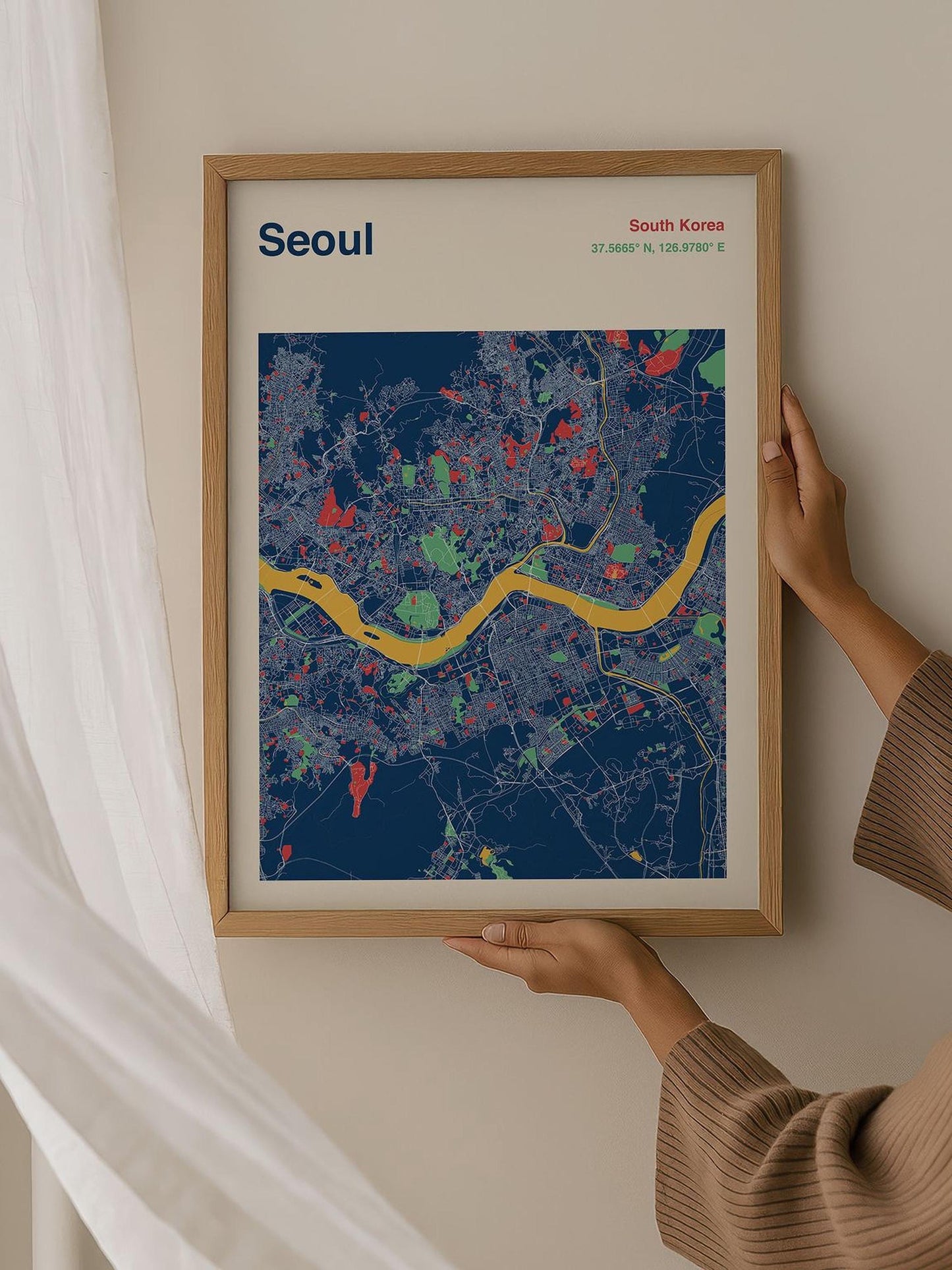 A person is holding up a framed map of Seoul, South Korea, which features a colorful and detailed representation of the city's streets and landmarks.