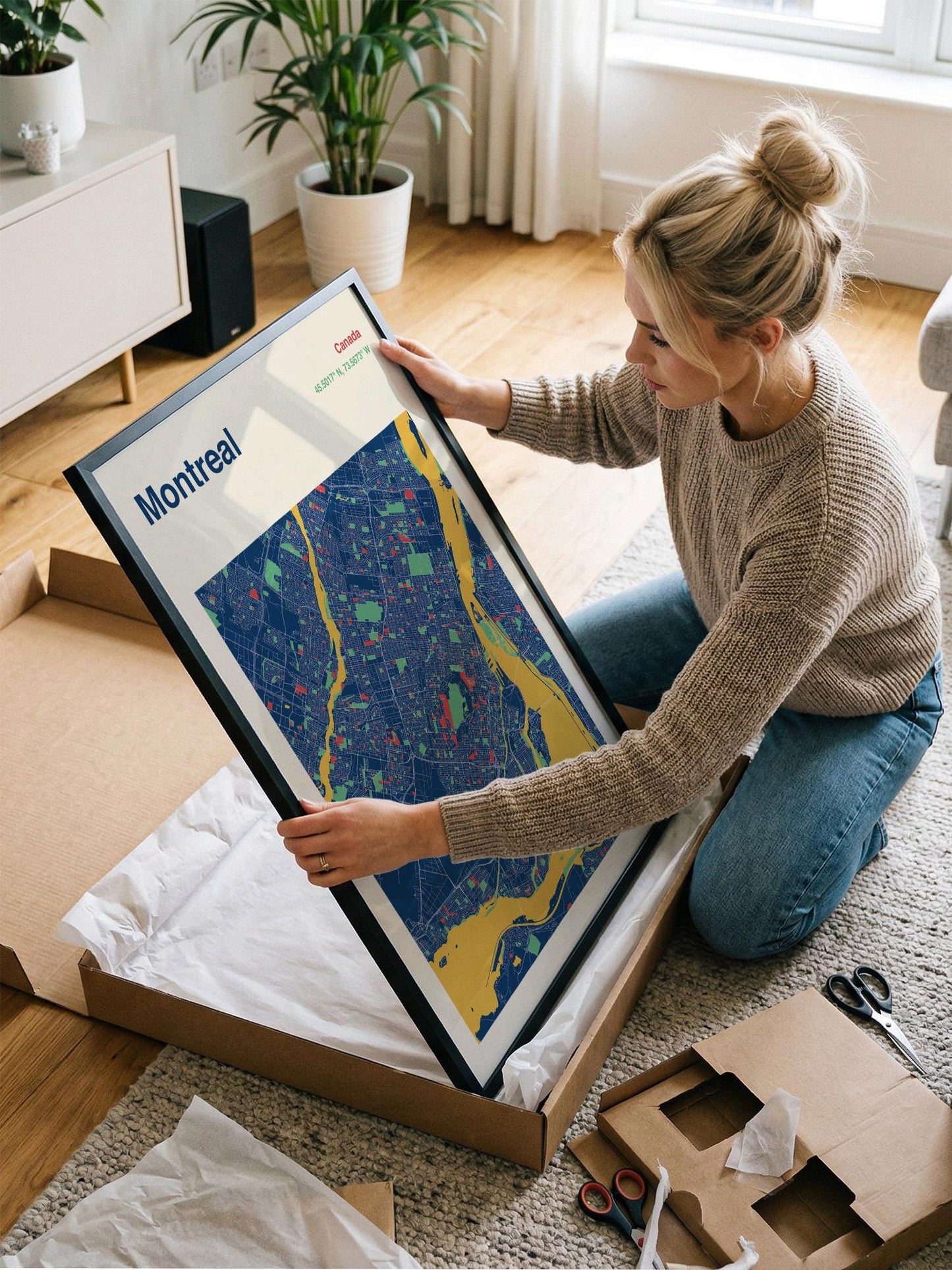 A woman is kneeling on the floor and holding a framed map of Montreal, which is a city in Canada.