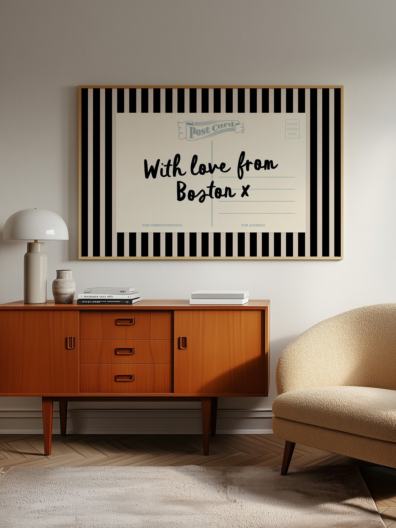 a vintage-style wooden cabinet with a lamp, a beige armchair, and a framed postcard with a message about love from Boston.