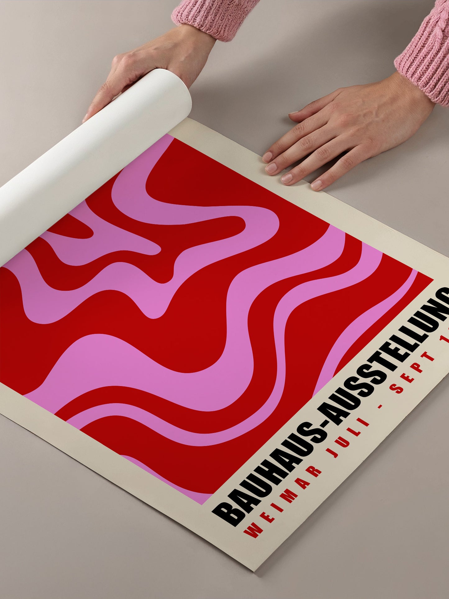 A person's hands are holding a roll of paper, which appears to be a poster or flyer with a bold, abstract design in red and pink colors.