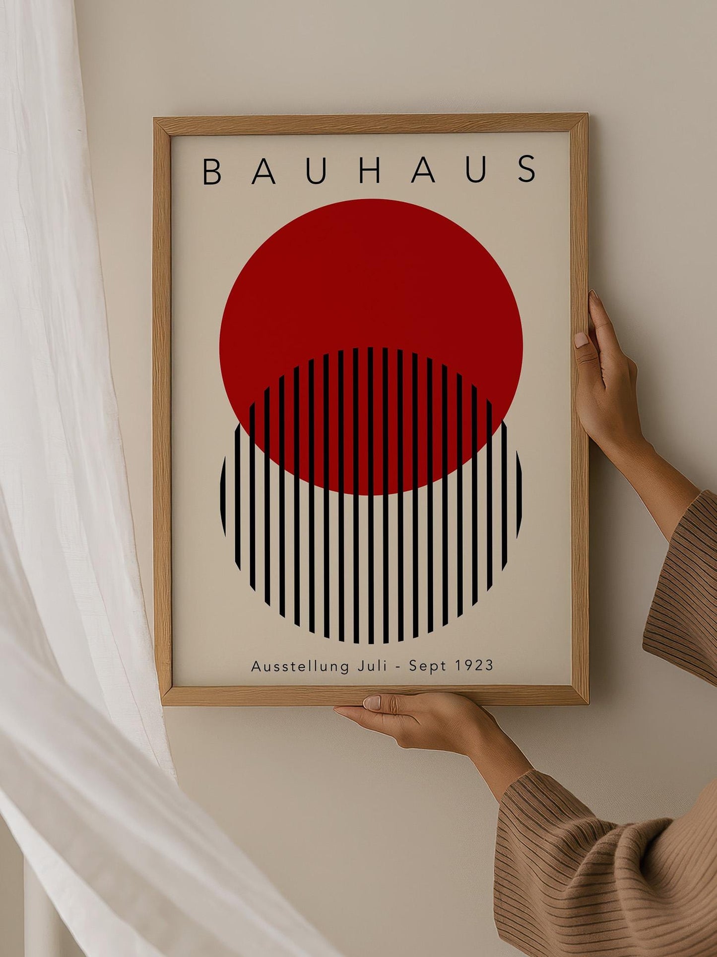A person is holding up a framed poster of the Bauhaus art style, featuring a bold red circle with black stripes.