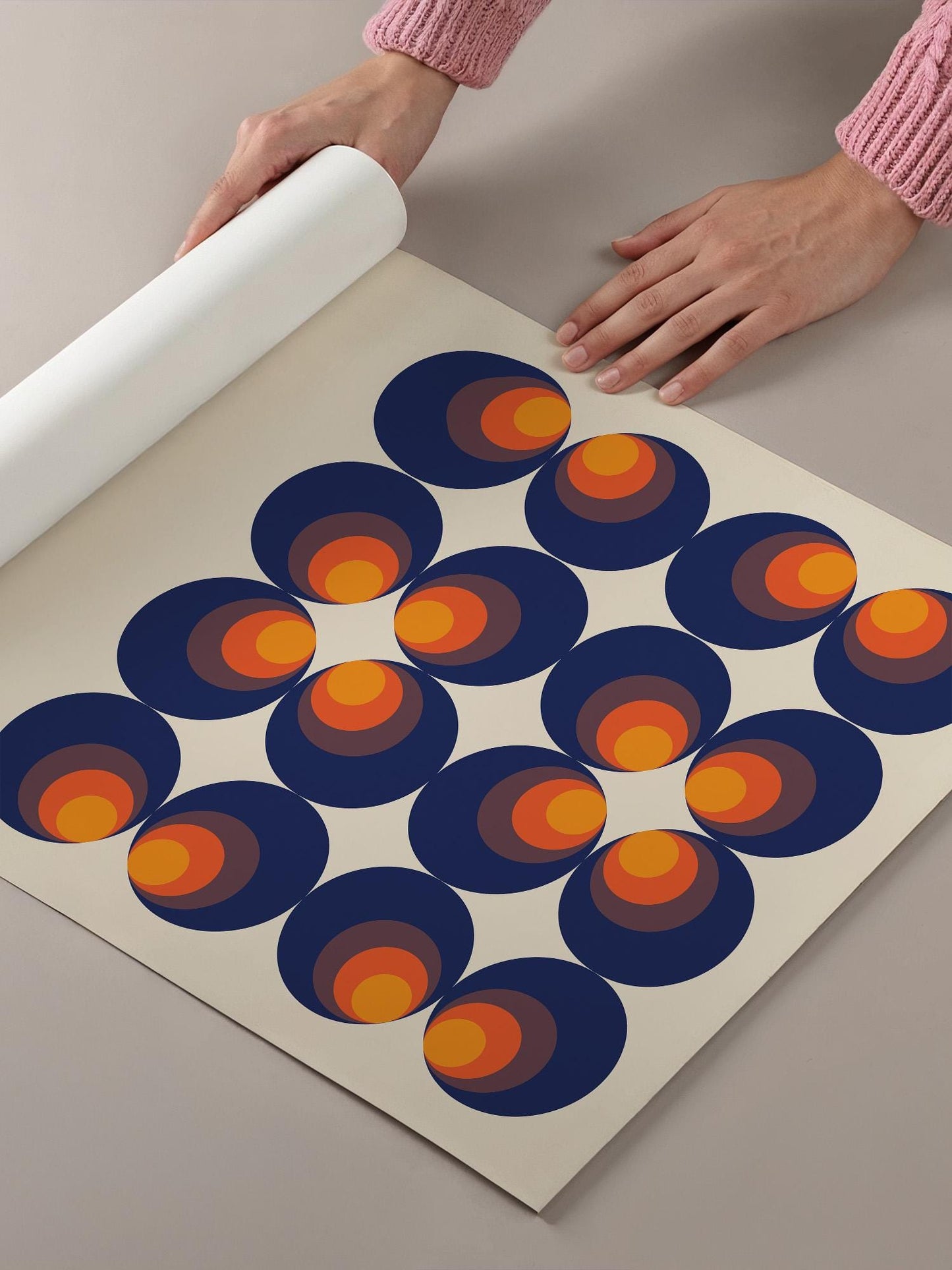 A person's hands are holding a roll of paper, which is laid out on a table with a pattern of overlapping circles in shades of blue and orange.