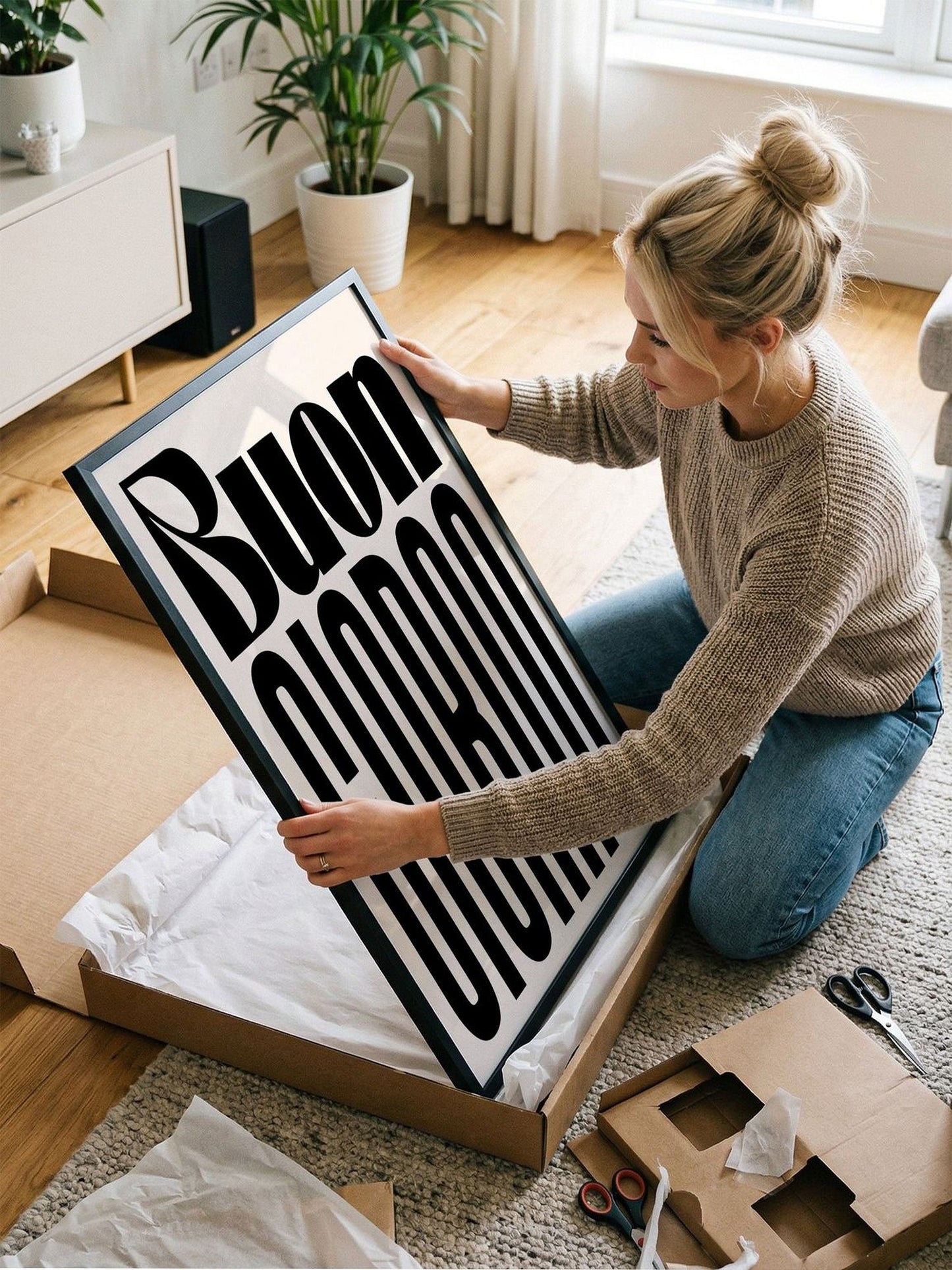 A woman is kneeling on the floor and holding a large framed poster with the word "Buon" written on it.