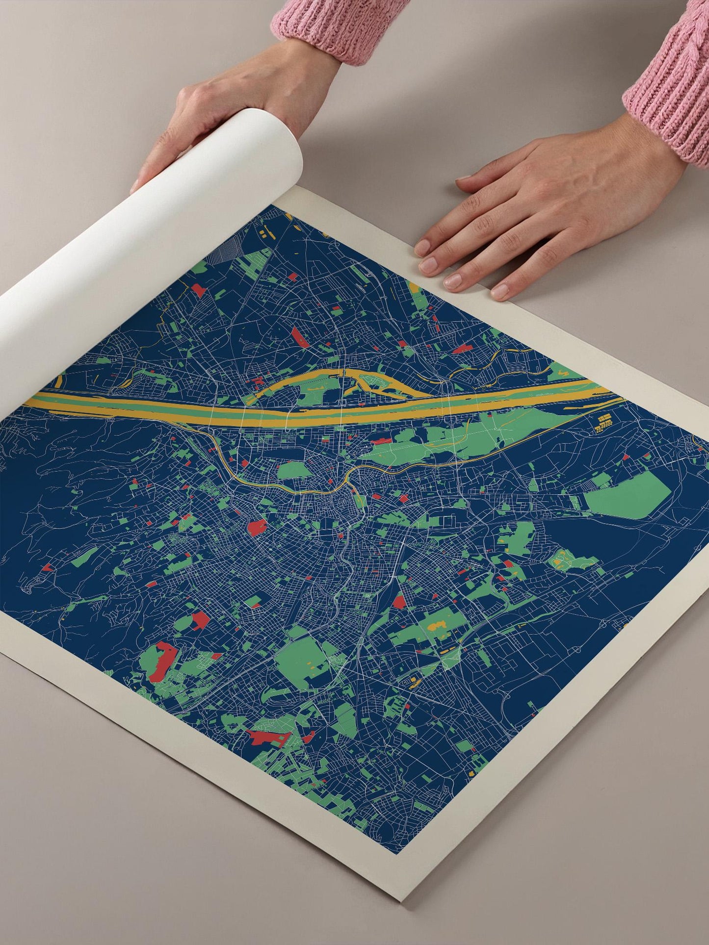 A person's hands are holding a roll of paper over a colorful map of a city, which appears to be a detailed and vibrant representation of the urban landscape.