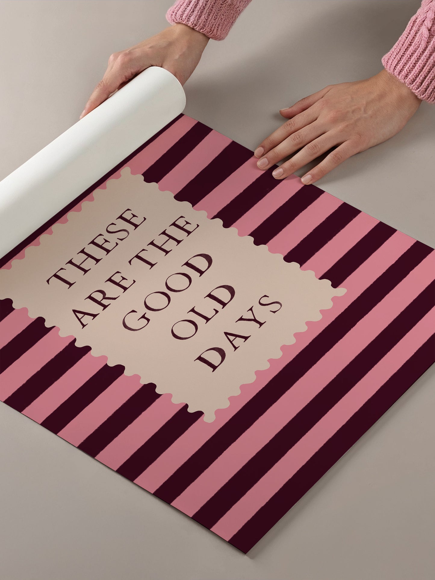 A person's hands are holding a roll of paper with the text "These are the good old days" printed on it, which is set against a background of pink and black striped patterns.