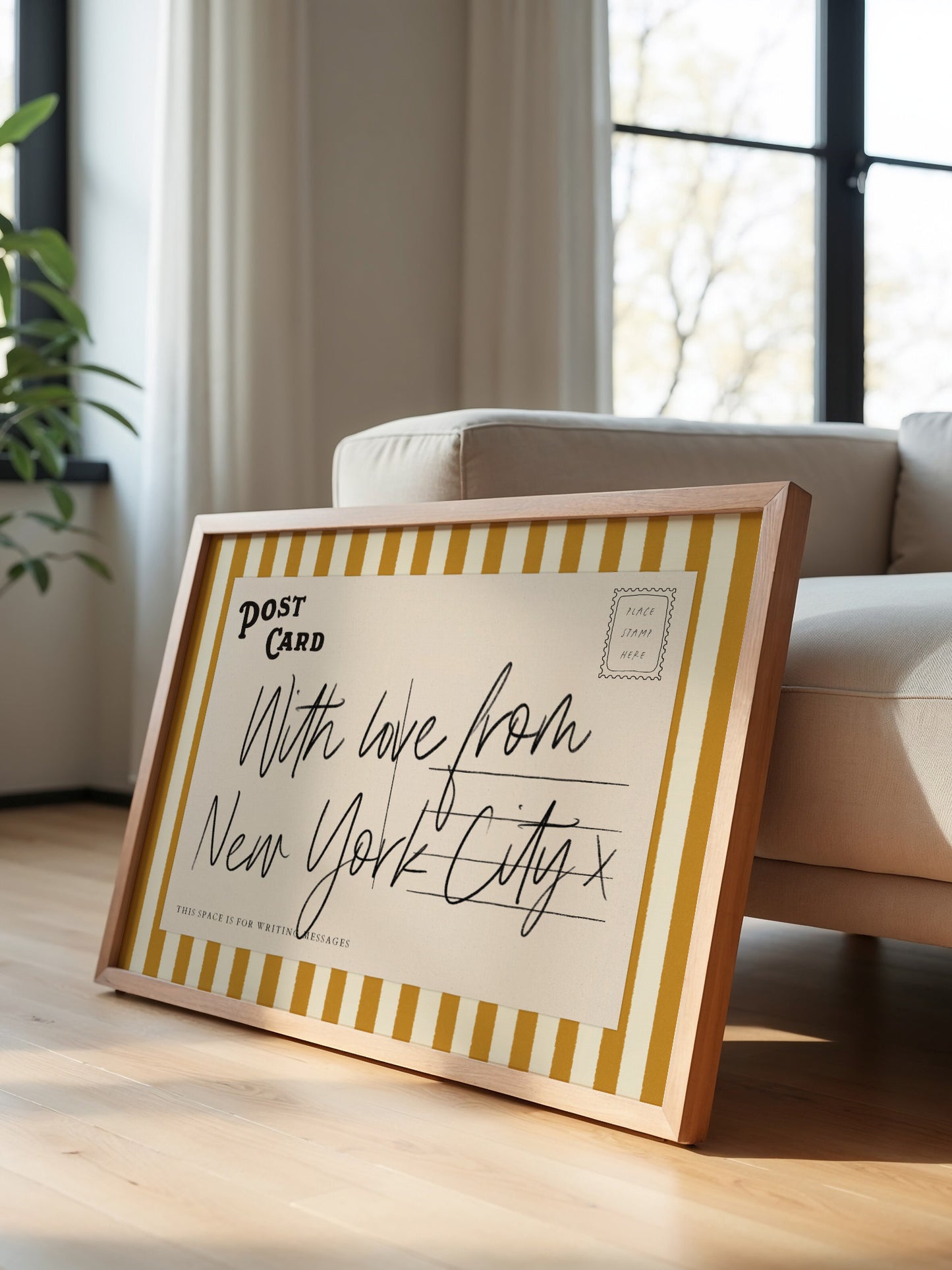A framed postcard with handwritten text is leaning against a white couch in a room with a window.
