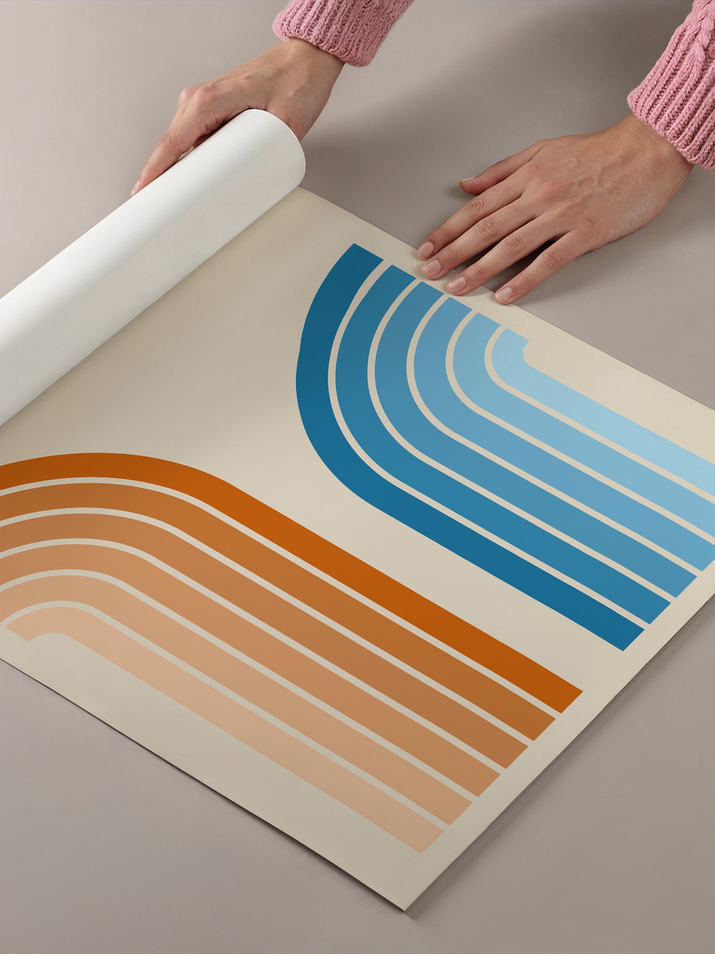 A person's hands are holding a roll of paper, which appears to be a poster or artwork with a geometric design featuring curved lines in various shades of blue and orange.