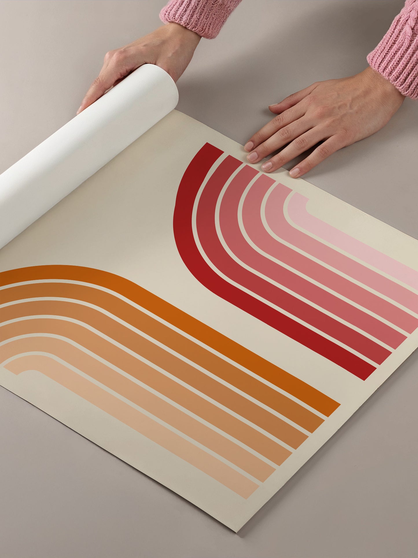 A person's hands are holding a roll of paper with a colorful abstract design featuring curved lines in shades of red, orange, and pink.