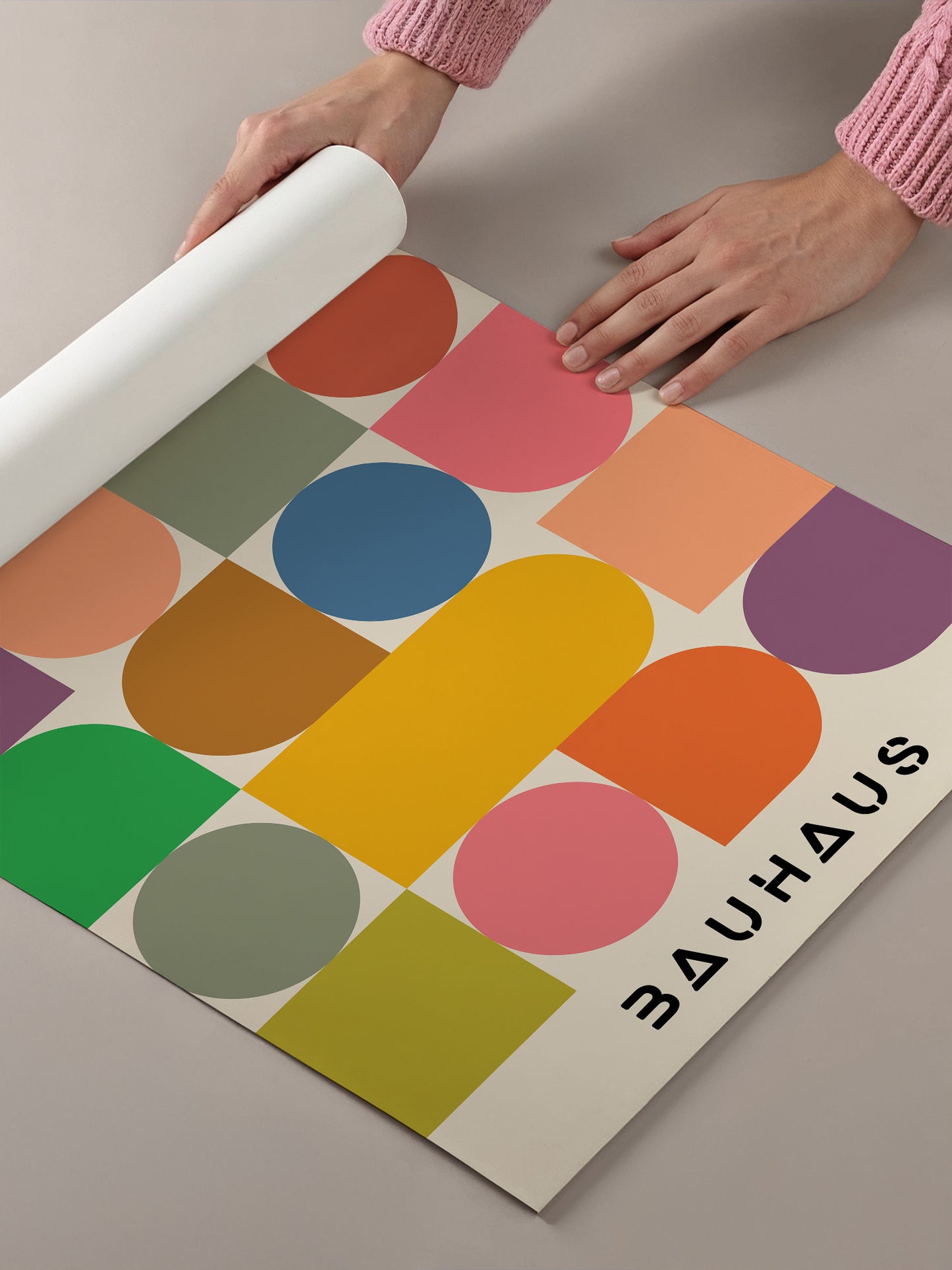 A person's hands are holding a roll of paper, which appears to be a poster or artwork featuring a geometric design with various shapes and colors.