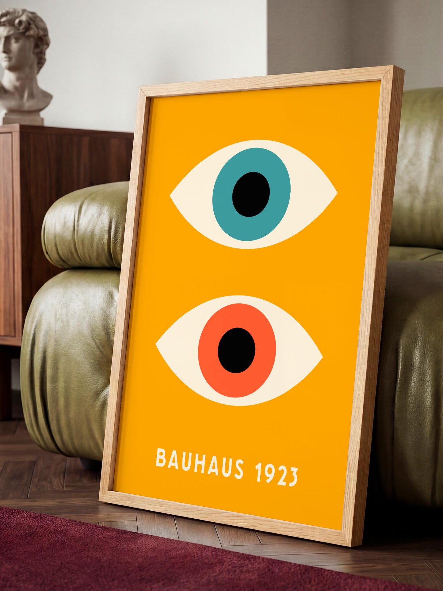a framed poster with a bold yellow background and two stylized eyes, one blue and one orange, positioned on a wooden floor.