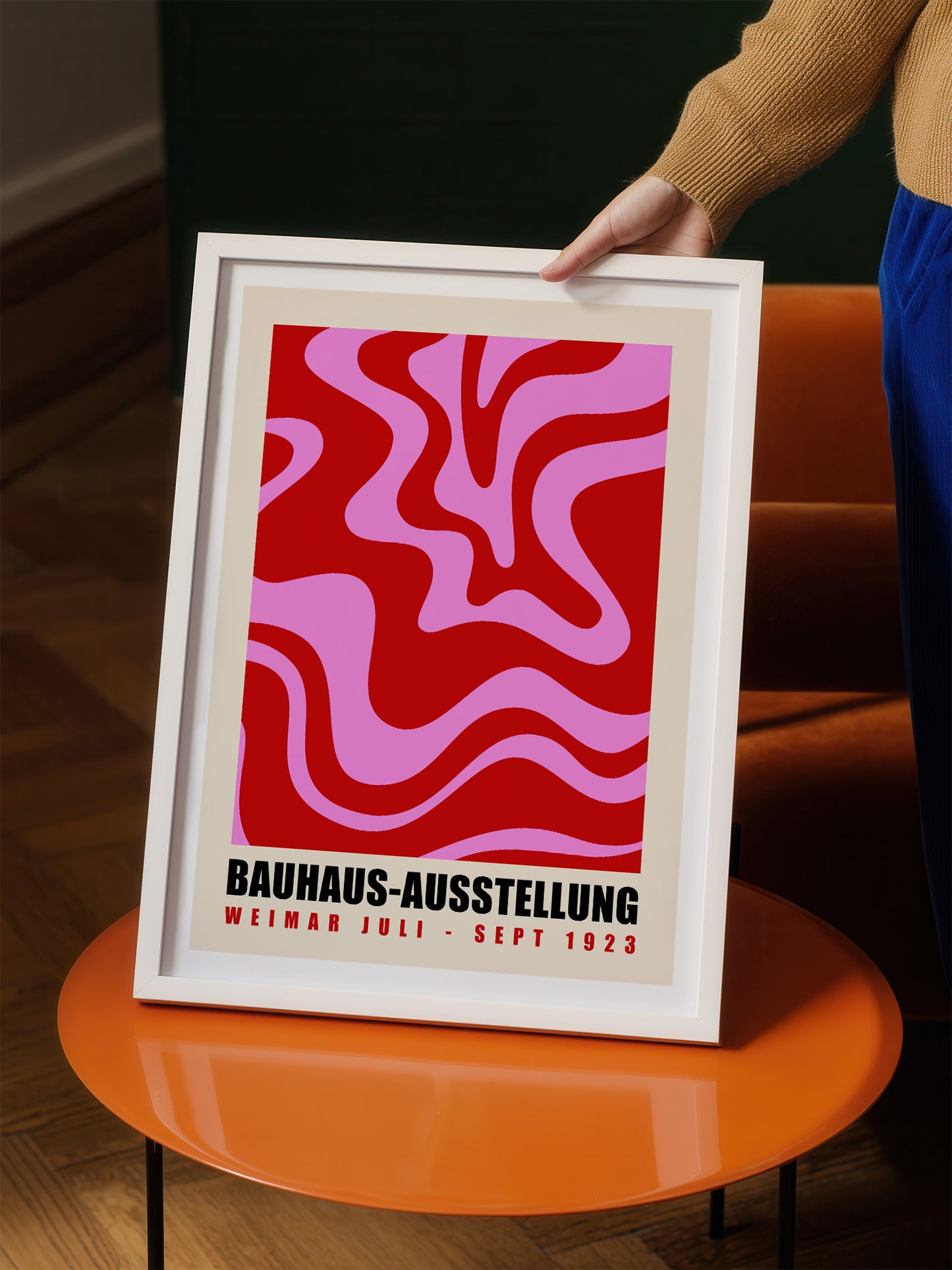 A person is holding up a framed poster with a bold, abstract design in red and pink colors.