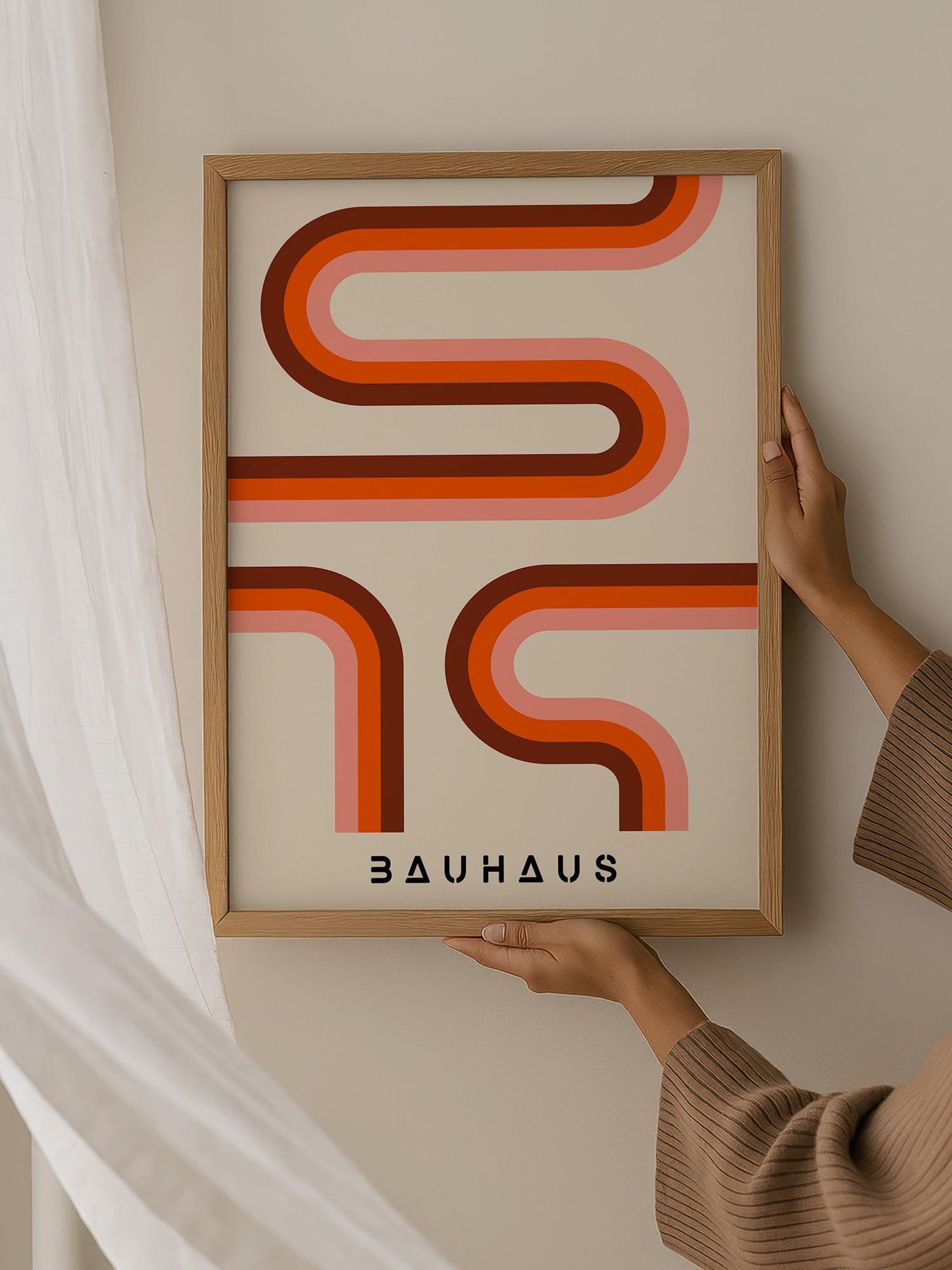 A person is holding up a framed poster with a bold, abstract design featuring curved lines in shades of orange and pink.