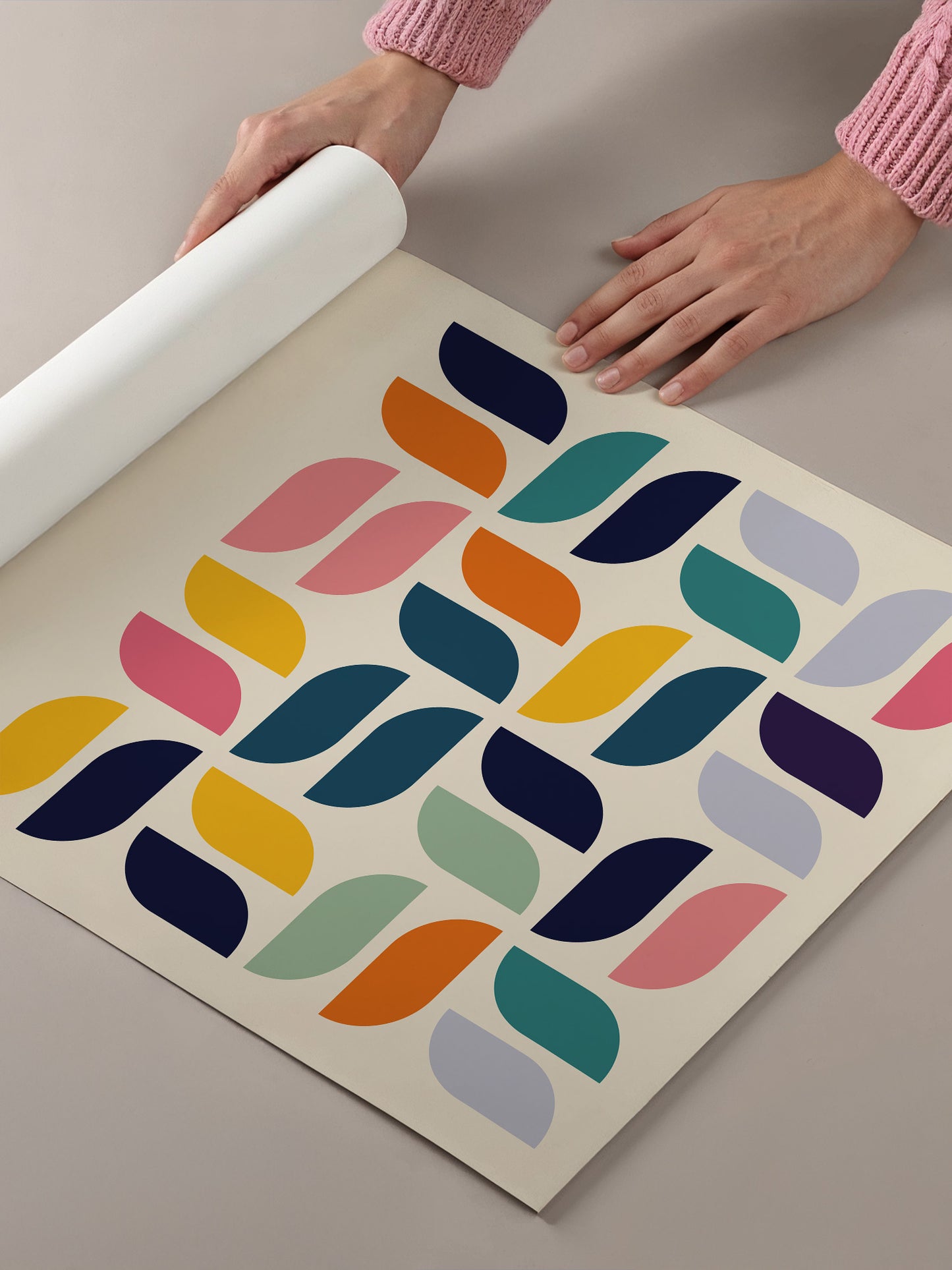A person's hands are holding a roll of paper, which appears to be a piece of paper with a colorful geometric pattern on it.