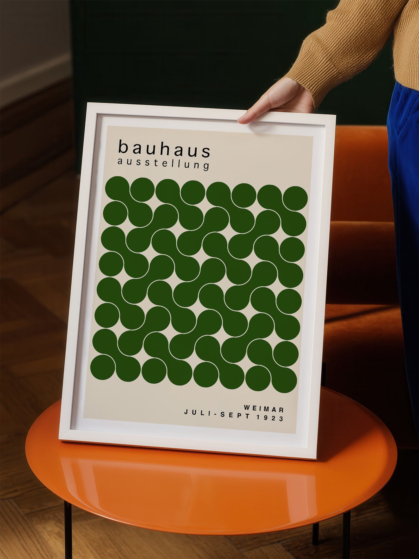 A person is holding up a framed poster with a repeating pattern of green circles on a white background.