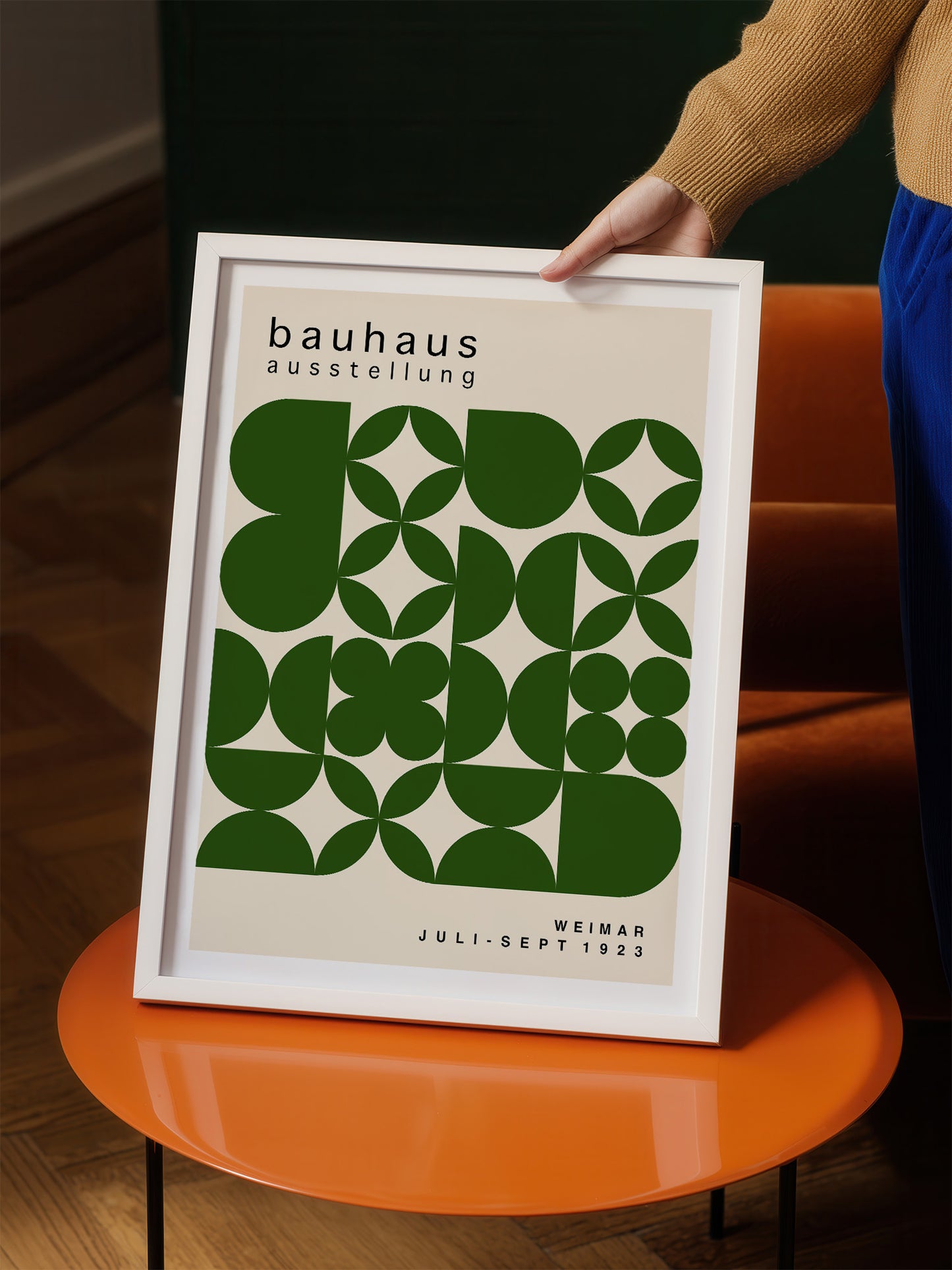 A person is holding up a framed poster with a geometric design in shades of green and white.