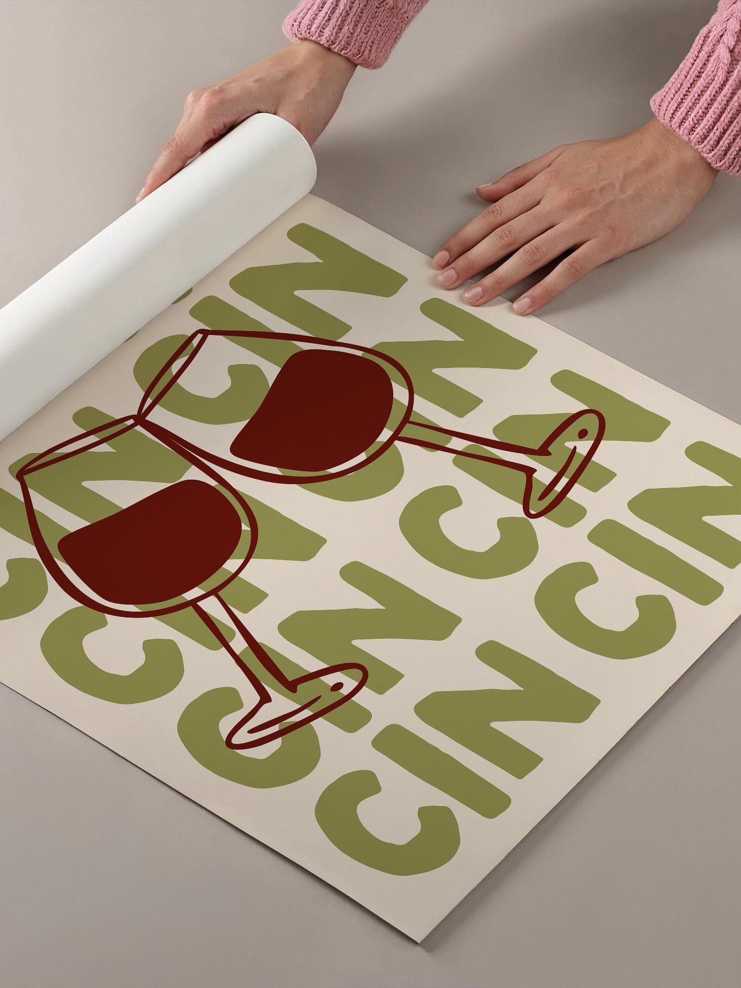 a person's hands holding a roll of paper, with a poster or sign featuring a wine glass design and the word "CINNAMON" printed on it.