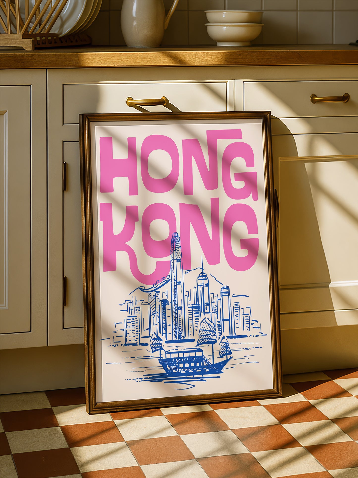 A framed poster of Hong Kong with a cityscape illustration is displayed on a checkered floor in a kitchen.