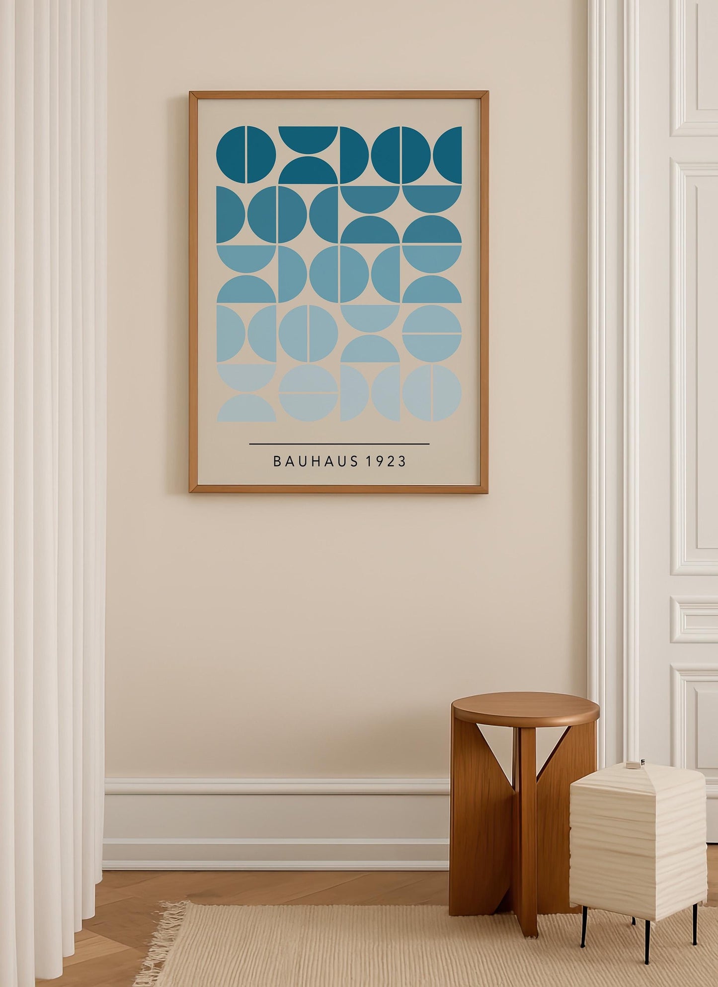 a minimalist interior design with a large framed poster of a geometric pattern in shades of blue and green hanging on a beige wall. Below the poster, there is a small wooden stool and a white lamp, creating a cozy and stylish atmosphere.