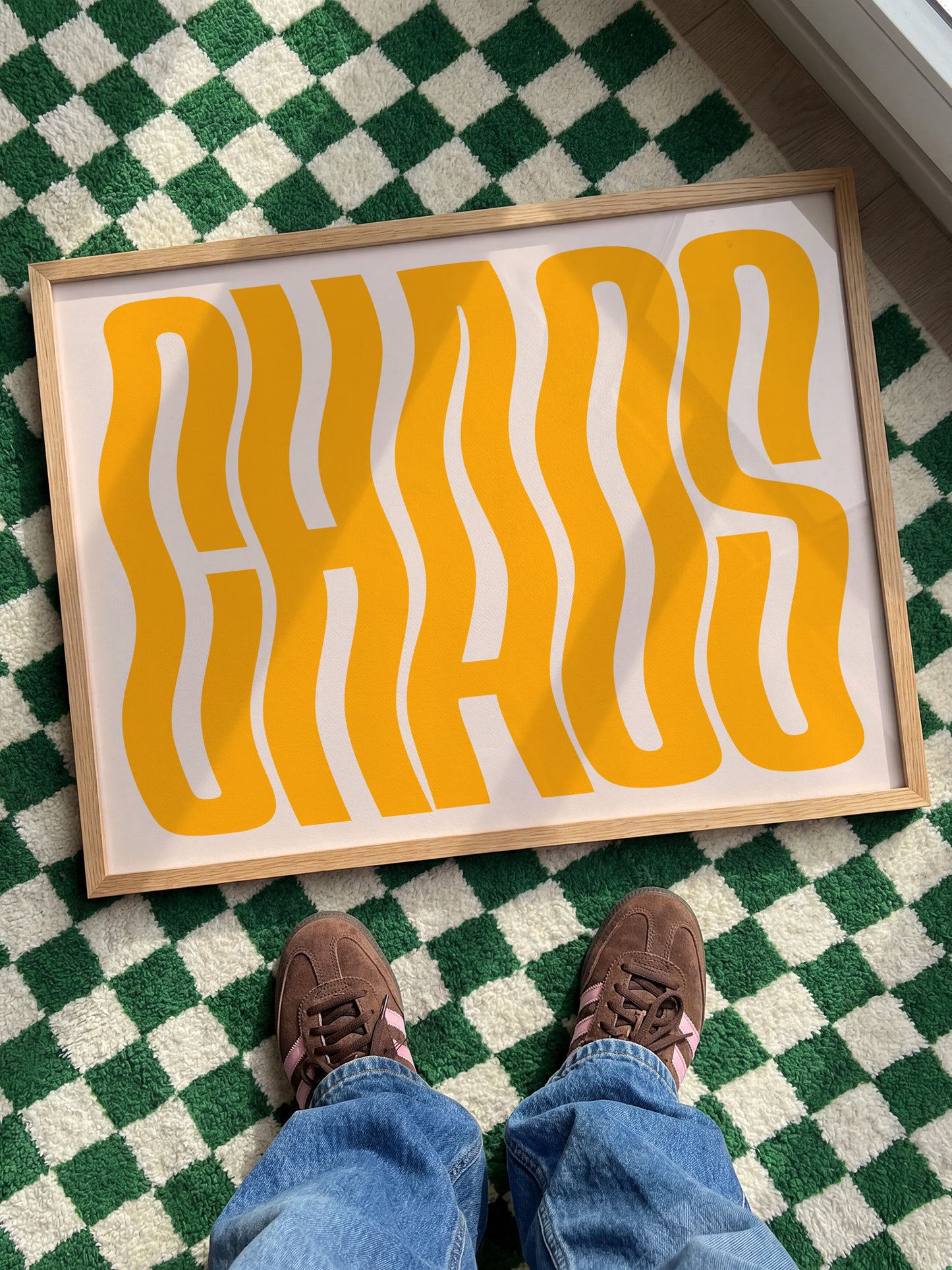 A person's feet standing on a checkered green and white rug, with a large framed text or graphic in the foreground.