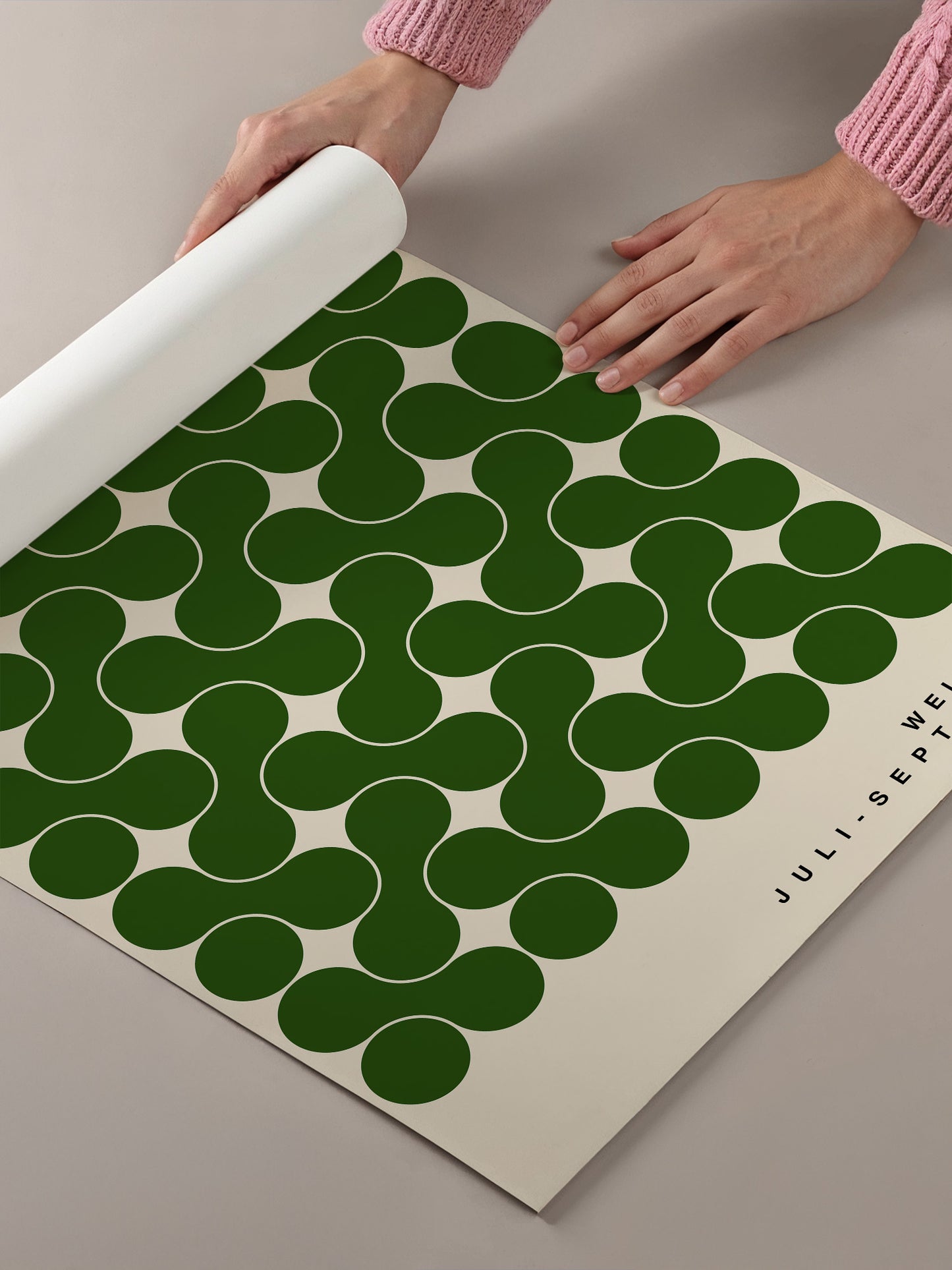 A person's hands are holding a roll of paper with a repeating pattern of green circles on a beige background.