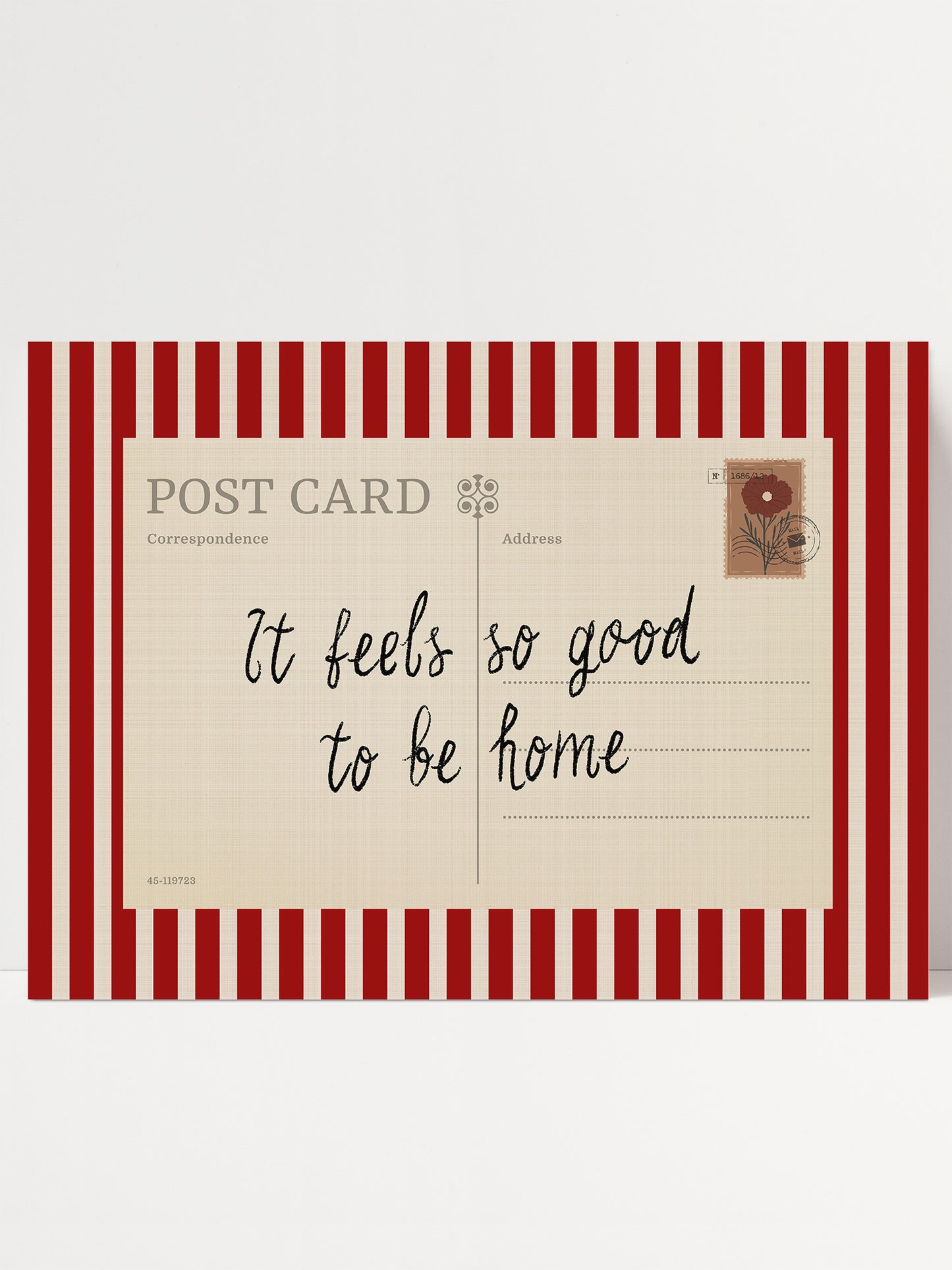 A postcard with a red and white striped border, featuring a handwritten message that reads "It feels so good to be home".