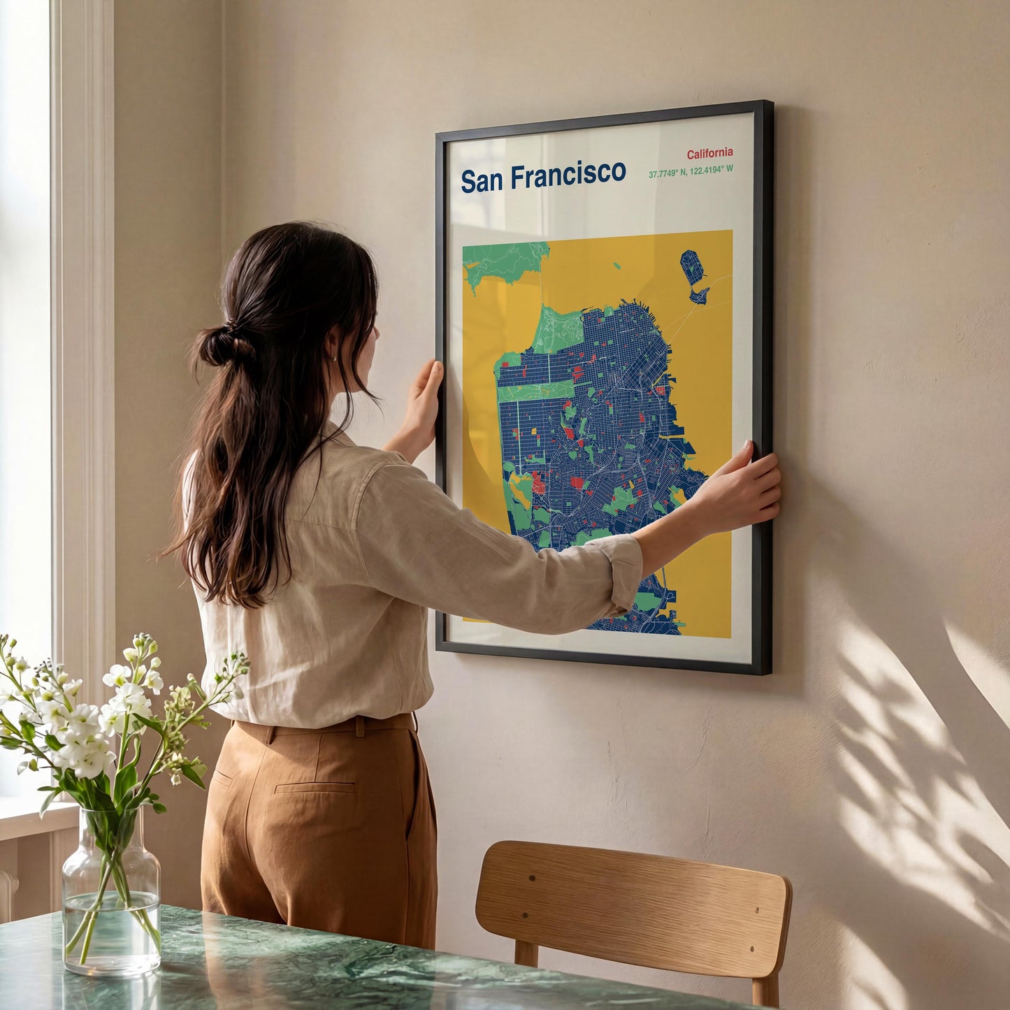 A woman is hanging a framed map of San Francisco on a wall.