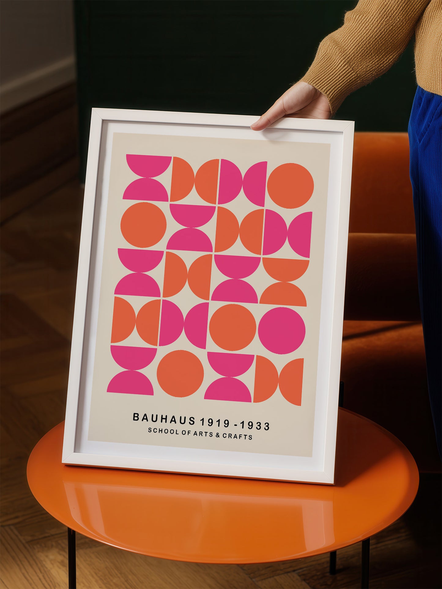 A person is holding up a framed poster with a geometric design featuring circles and lines in various shades of pink and orange.