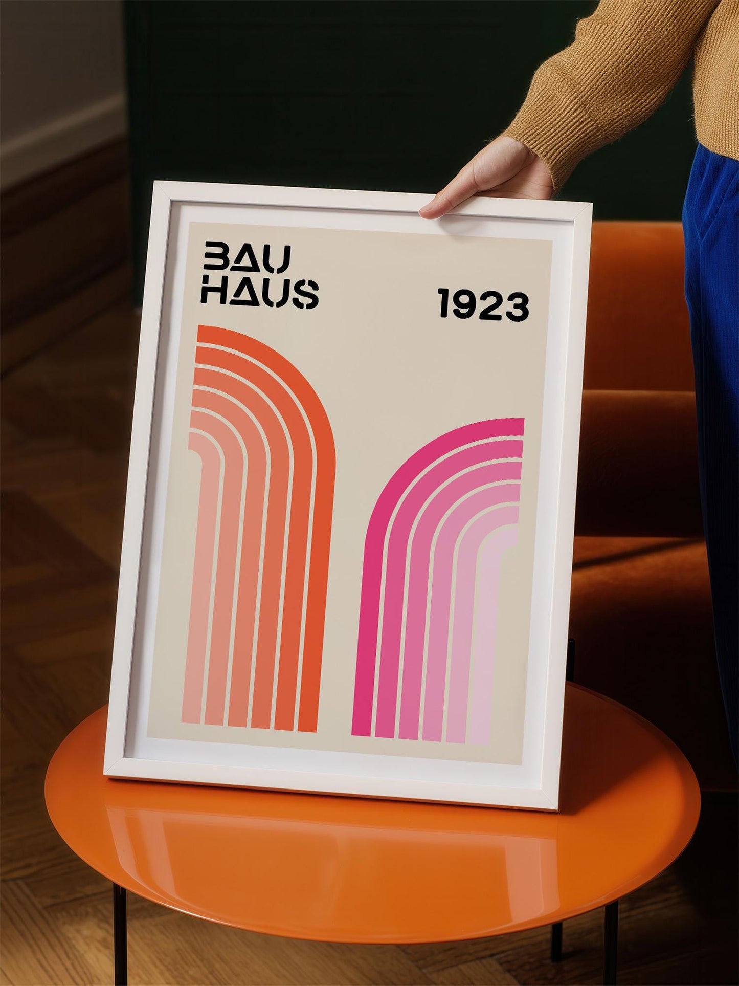 A person is holding a framed poster with the text "BAU HAUS 1923" and two abstract geometric shapes in pink and orange.