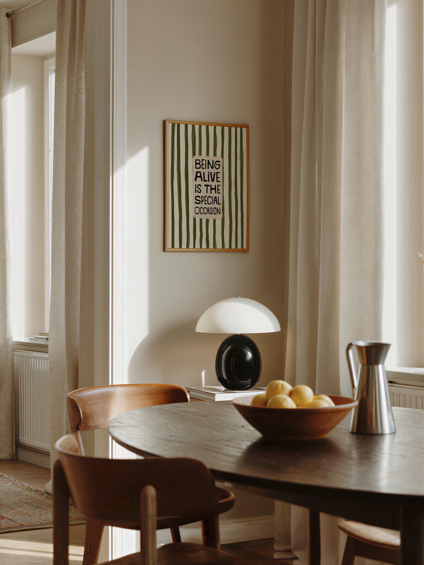 a cozy dining area with a wooden table, two chairs, and a bowl of fruit. A framed quote on the wall says "Being alive is the special occasion".