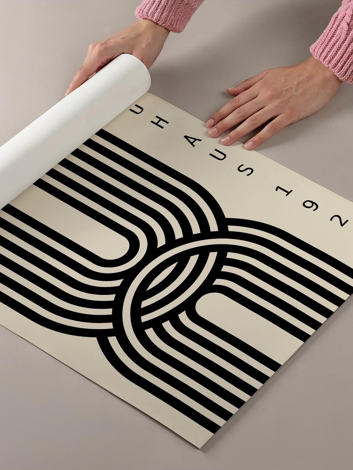 A person's hands are holding a roll of paper, which appears to be a poster or artwork with a black and white abstract design.
