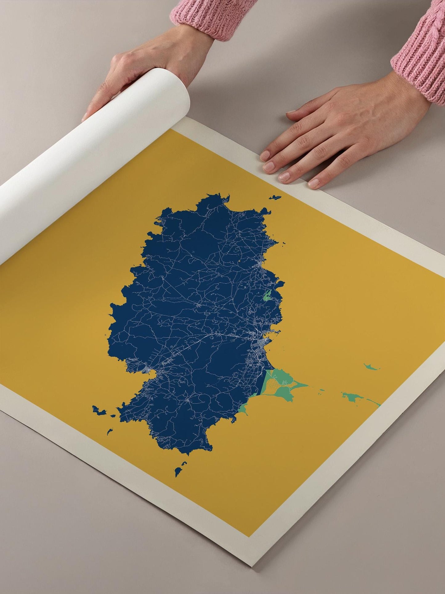 A person's hands are holding a roll of paper over a map of a large area, which appears to be a map of a country or region.
